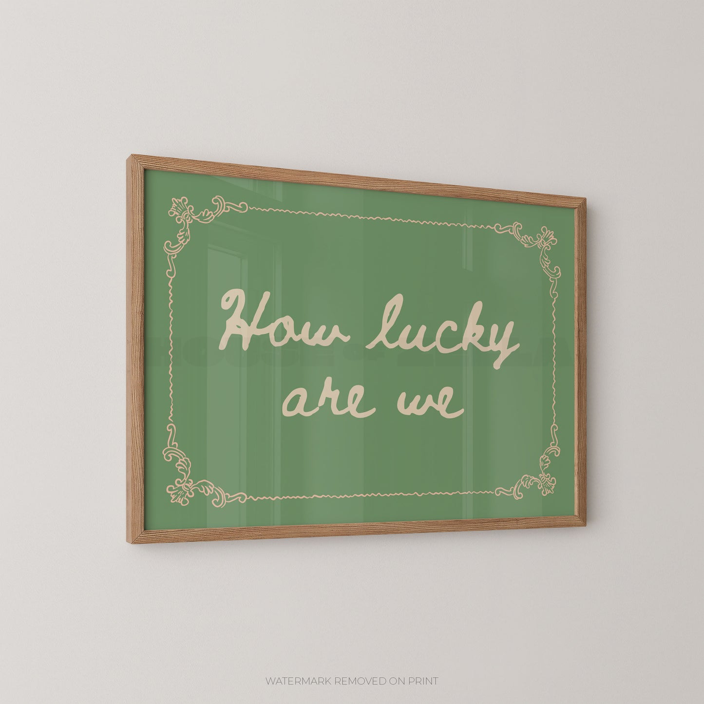 A framed wall art print with a green background, cream script text reading 'How lucky are we,' and a light wood frame, shown hanging on a plain light wall.