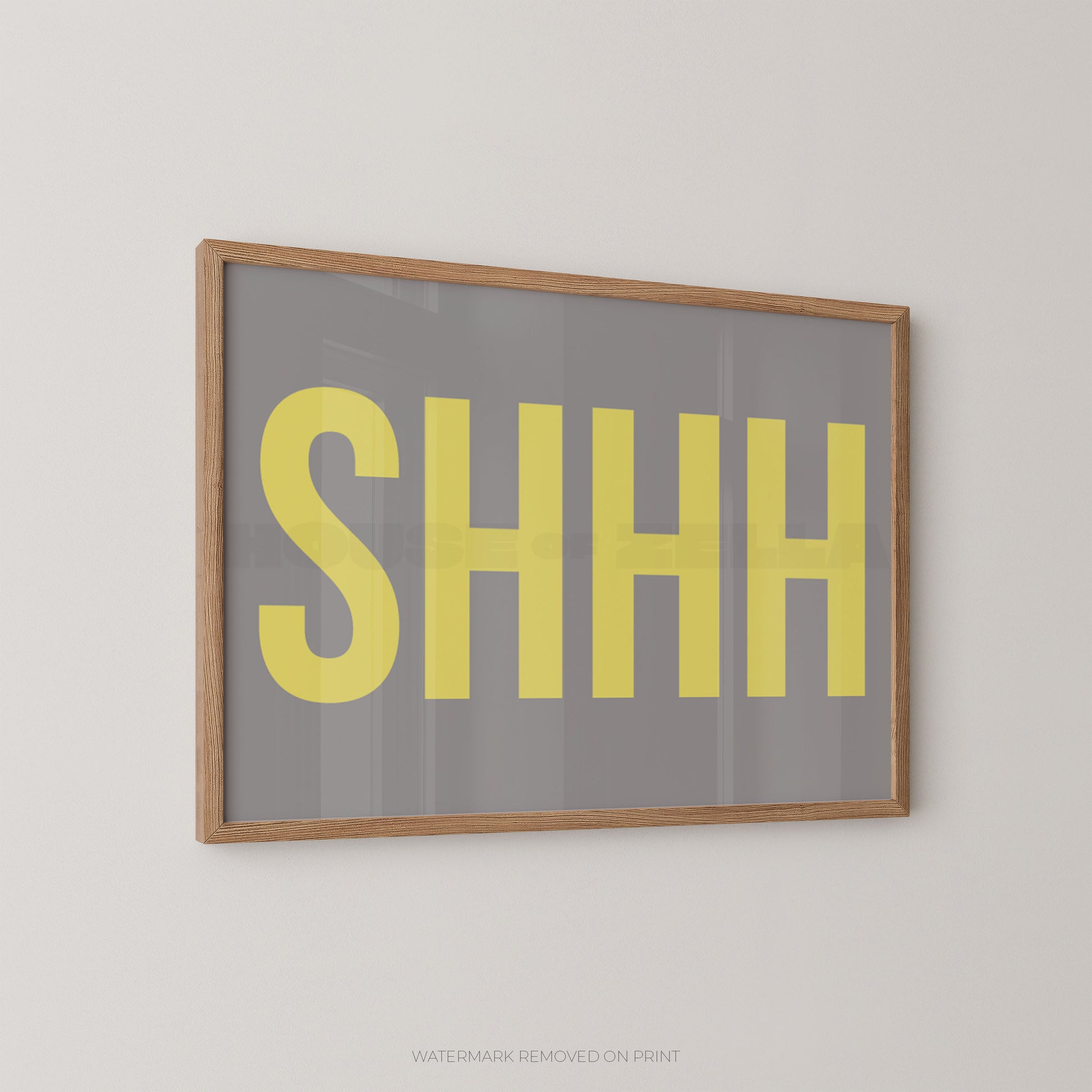 Framed wall art print with the word 'SHHH' in large yellow letters on a gray background, shown hanging on a light gray wall.