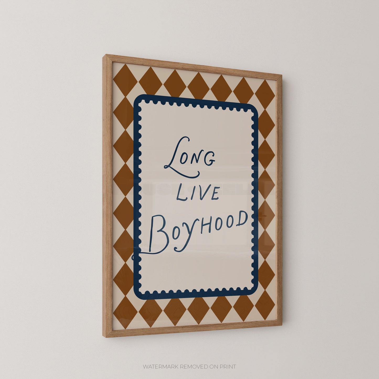 Framed wall art with the phrase 'Long Live Boyhood' in blue script inside a cream central panel, surrounded by a navy scalloped border and a tan-and-cream diamond pattern, shown in a light wood frame on a white wall.