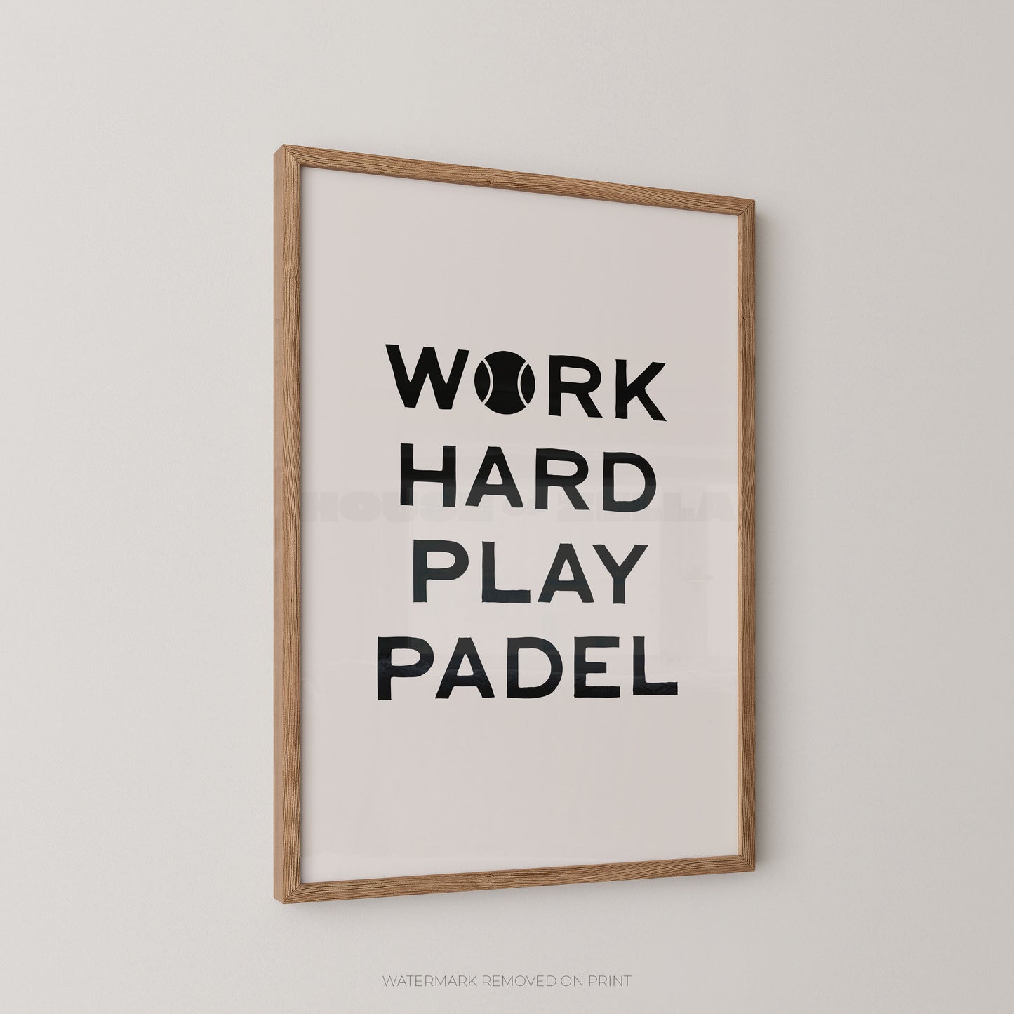 A framed wall art print with the text 'WORK HARD PLAY PADEL' in black on a white background, shown hanging on a light gray wall. The print has a light wood frame.