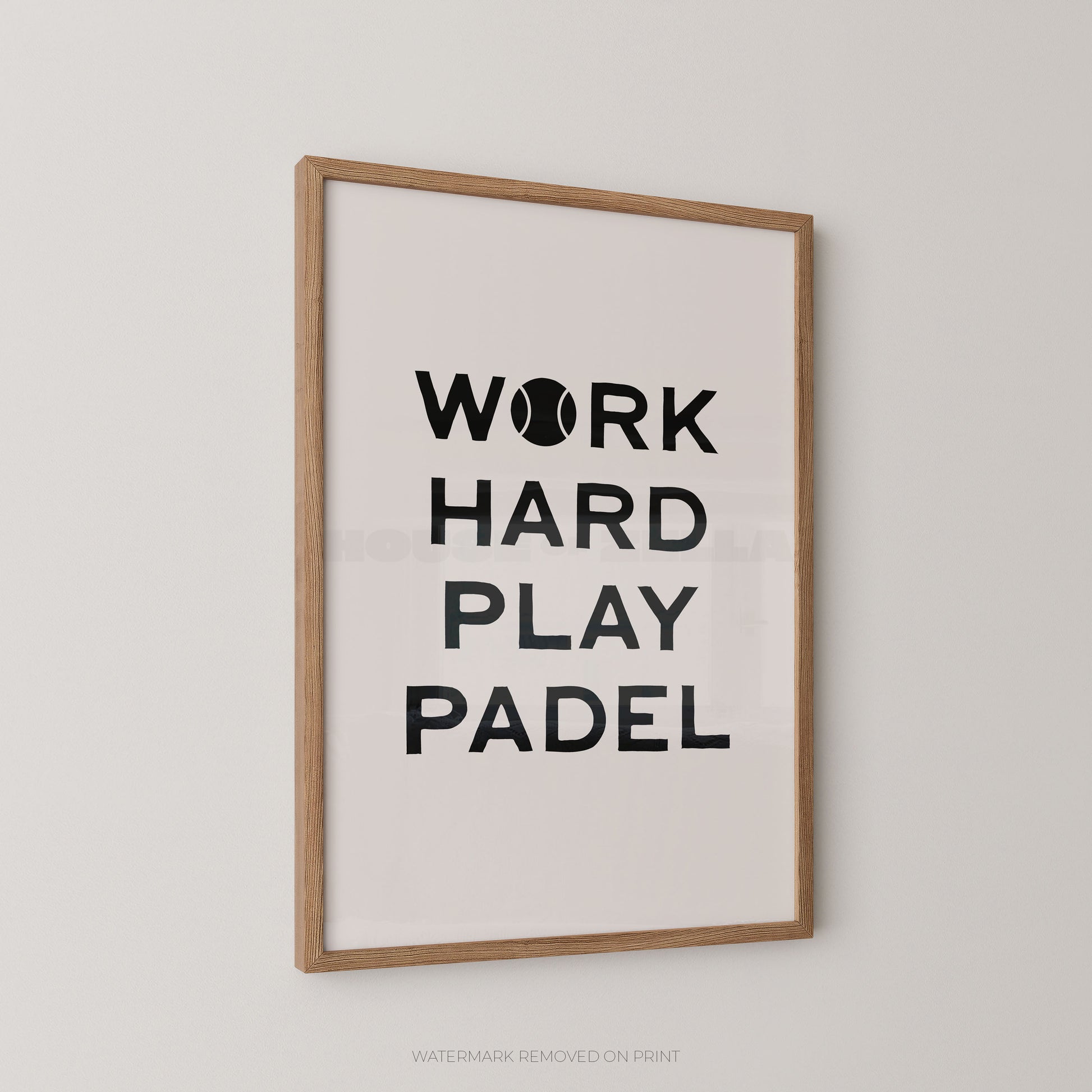 A framed wall art print with the text 'WORK HARD PLAY PADEL' in black on a white background, shown hanging on a light gray wall. The print has a light wood frame.