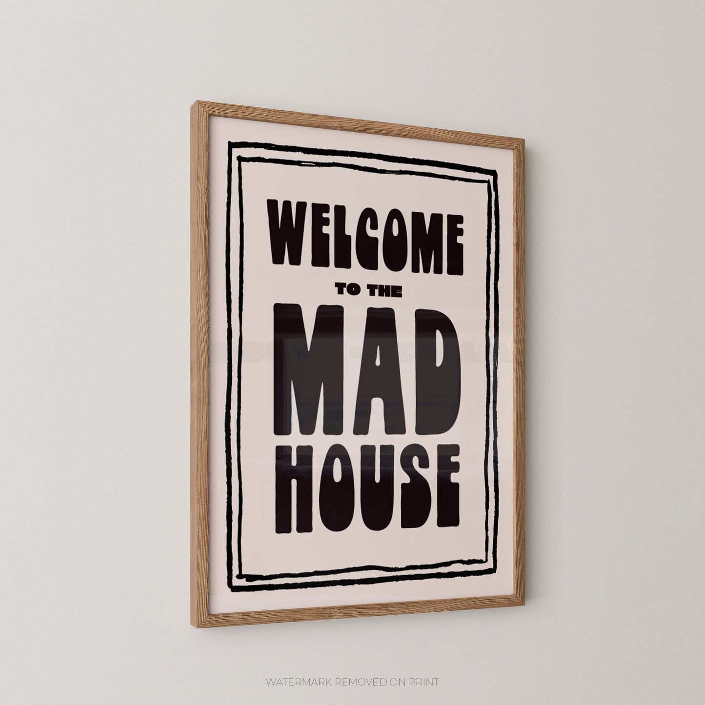 Framed wall art print with the text 'WELCOME TO THE MAD HOUSE' in bold black lettering on a cream background, enclosed in a light wood frame and shown hanging on a light gray wall.