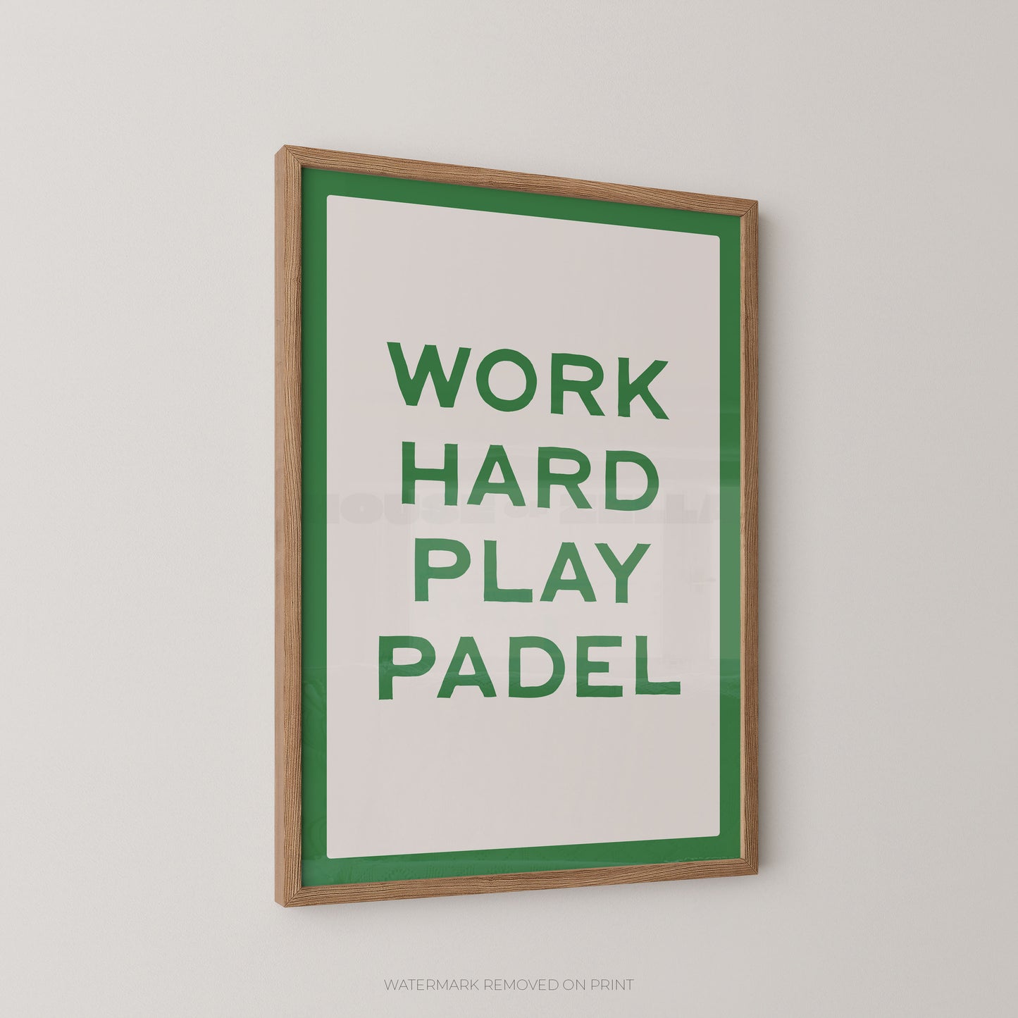 A framed typographic wall print with the words “WORK HARD PLAY PADEL” in green on a white background, bordered by a green inner frame and a natural wood outer frame, shown hanging on a light gray wall.