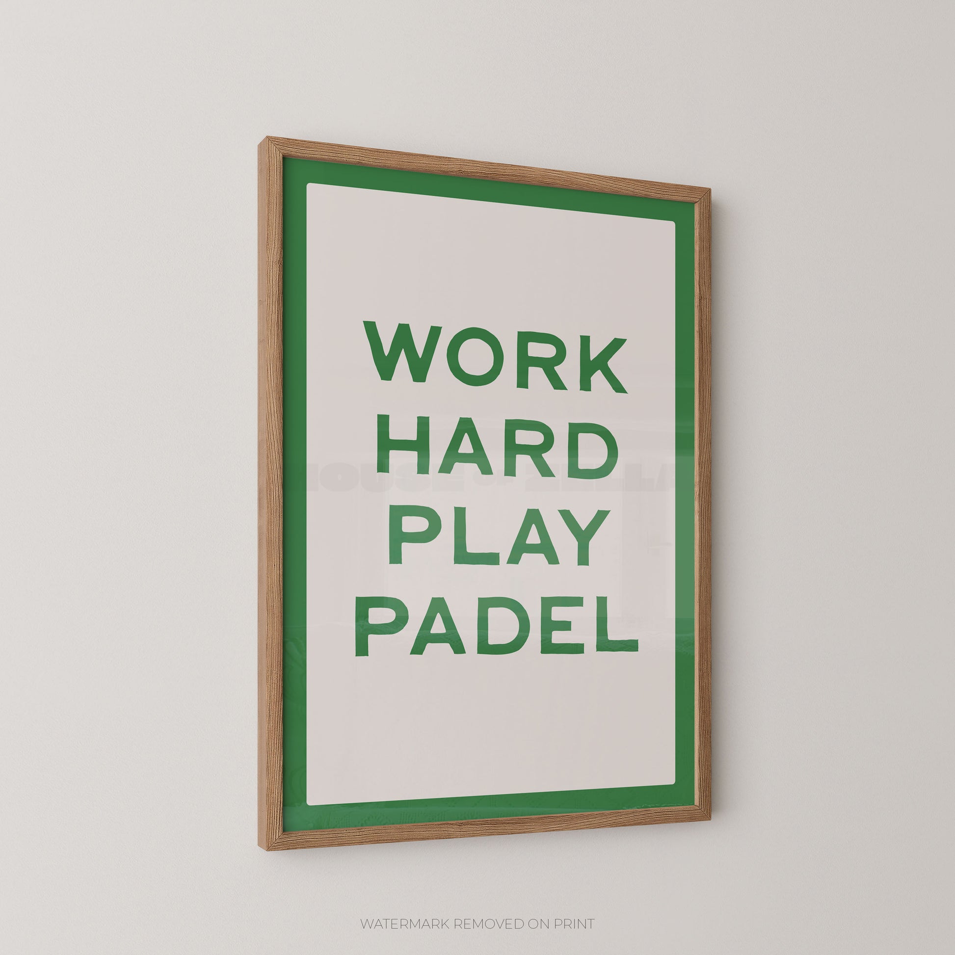 A framed typographic wall print with the words “WORK HARD PLAY PADEL” in green on a white background, bordered by a green inner frame and a natural wood outer frame, shown hanging on a light gray wall.