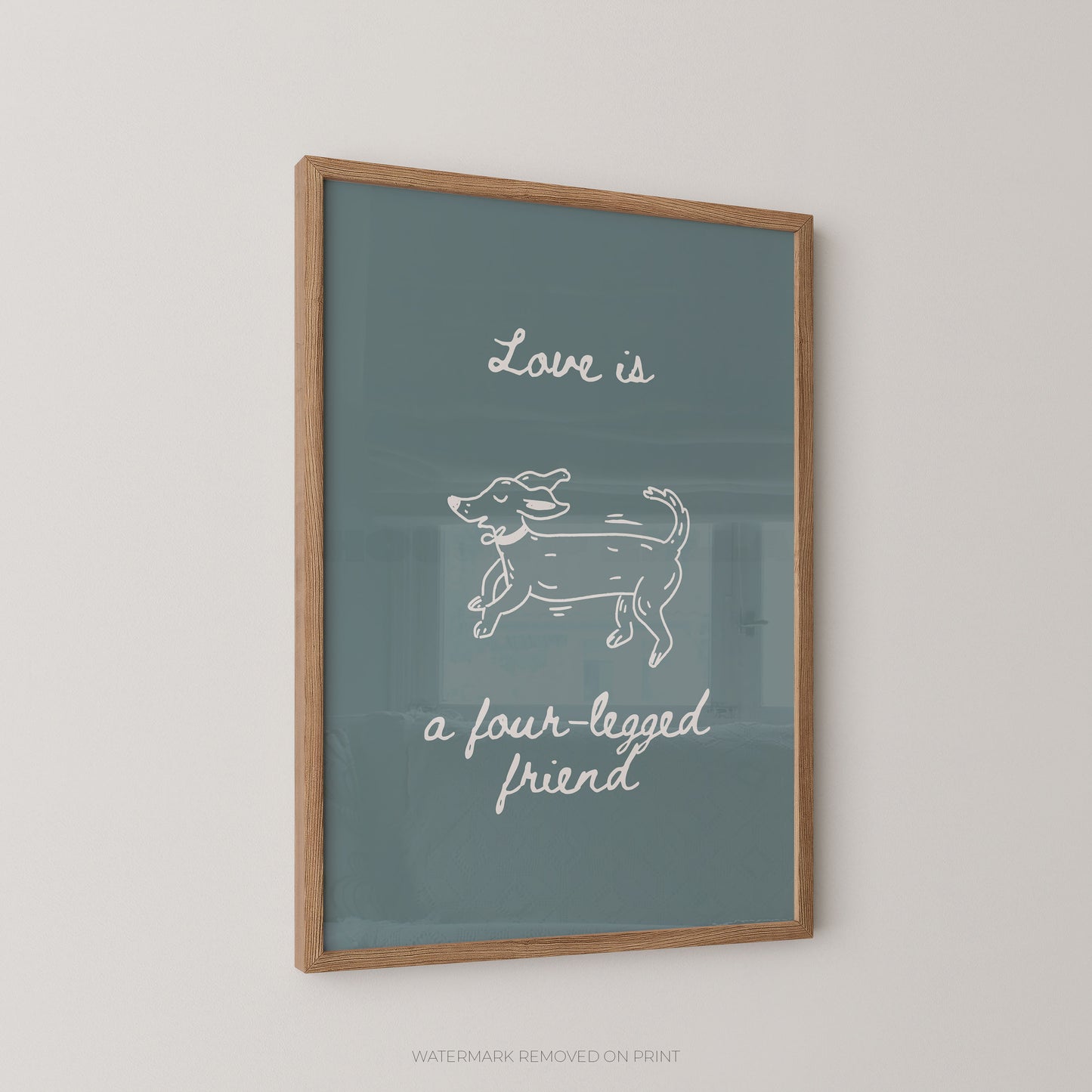 Framed wall art print with a muted blue-green background, white script text reading 'Love is a four-legged friend,' and a simple white line drawing of a dog, shown in a light wood frame against a light wall.