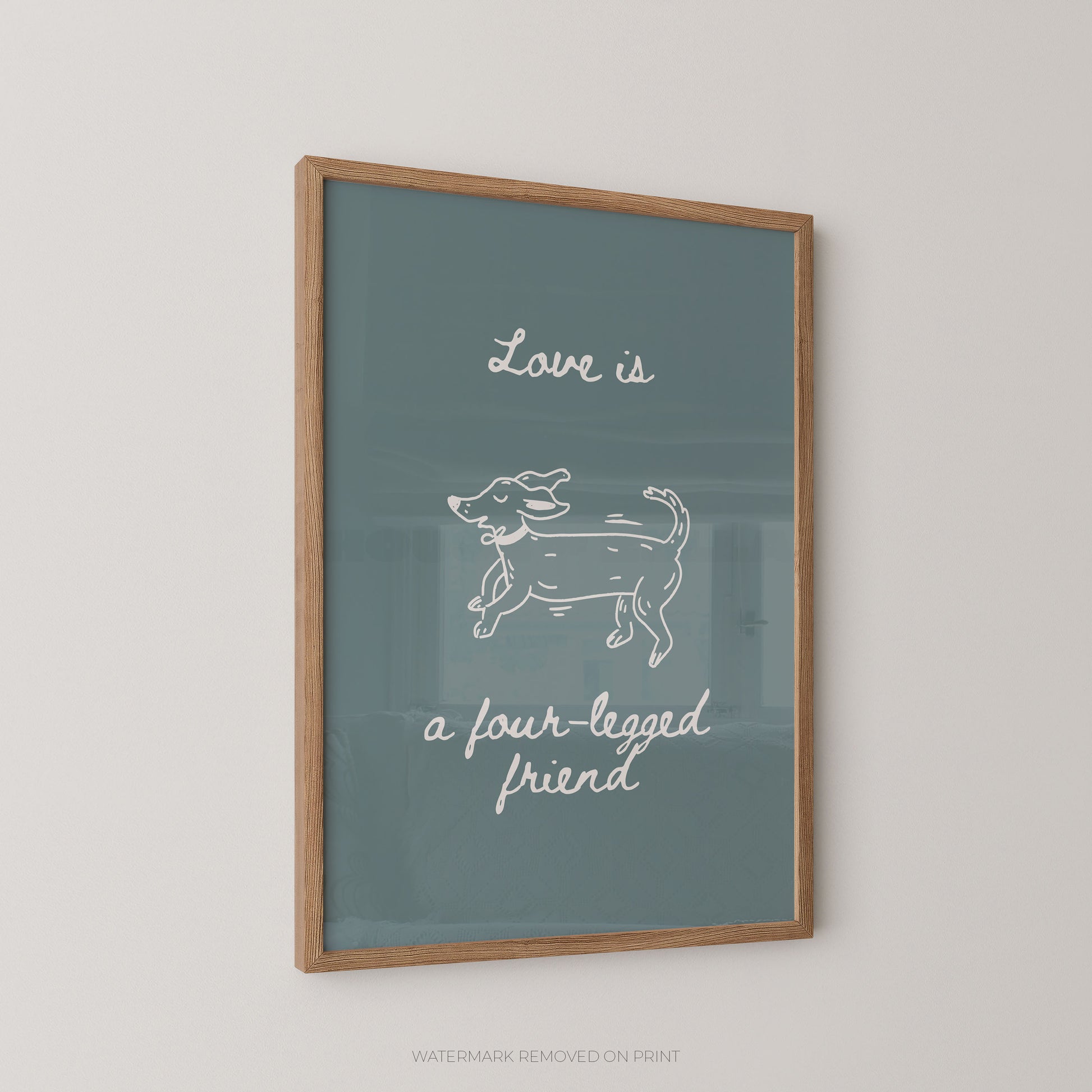 Framed wall art print with a muted blue-green background, white script text reading 'Love is a four-legged friend,' and a simple white line drawing of a dog, shown in a light wood frame against a light wall.