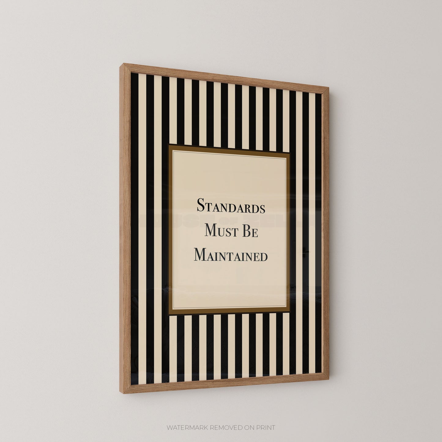 A framed wall art print with vertical black and cream stripes around a central cream panel that reads 'STANDARDS MUST BE MAINTAINED' in black serif text, shown hanging on a light gray wall.