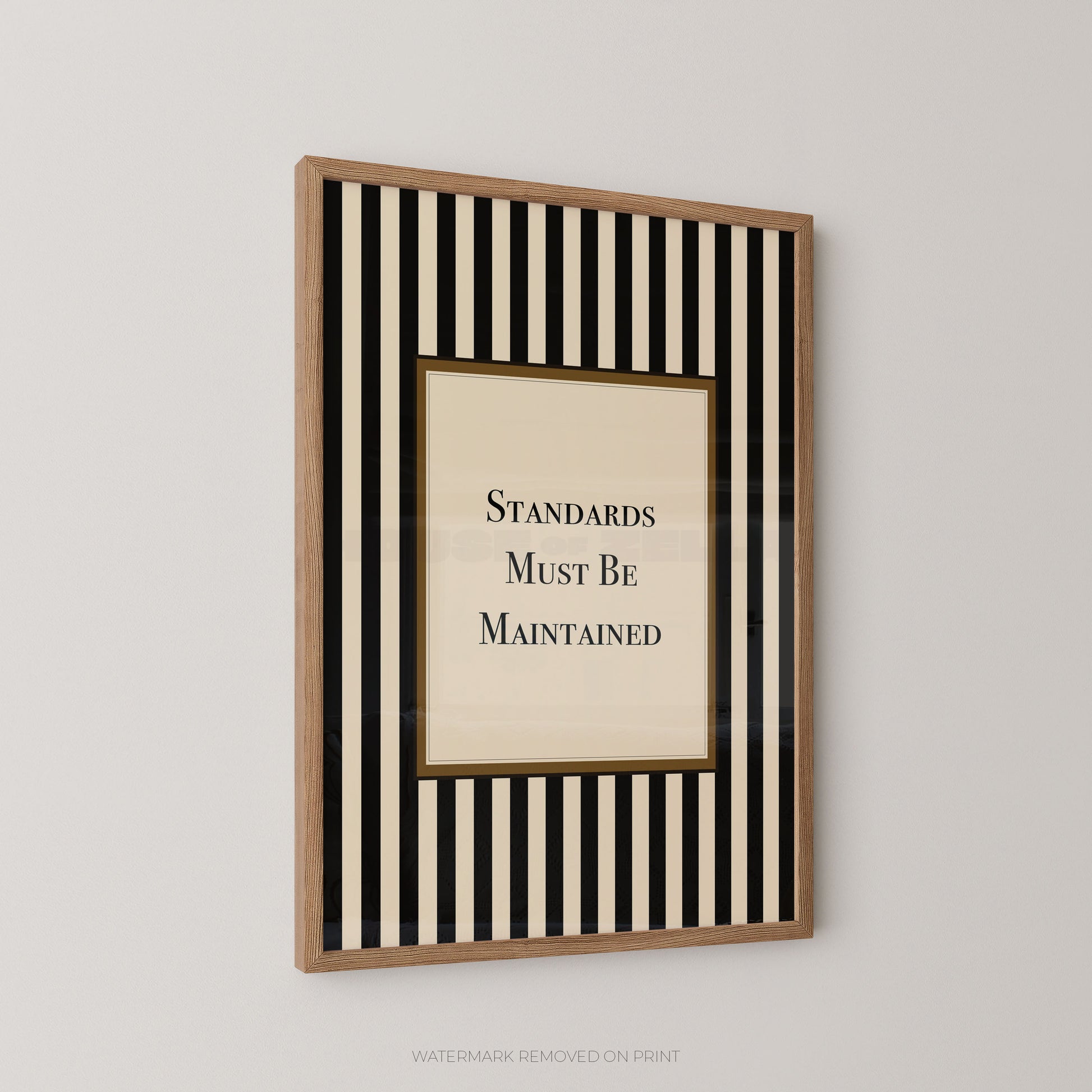 A framed wall art print with vertical black and cream stripes around a central cream panel that reads 'STANDARDS MUST BE MAINTAINED' in black serif text, shown hanging on a light gray wall.