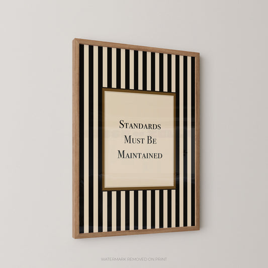 A framed wall art print with vertical black and cream stripes around a central cream panel that reads 'STANDARDS MUST BE MAINTAINED' in black serif text, shown hanging on a light gray wall.