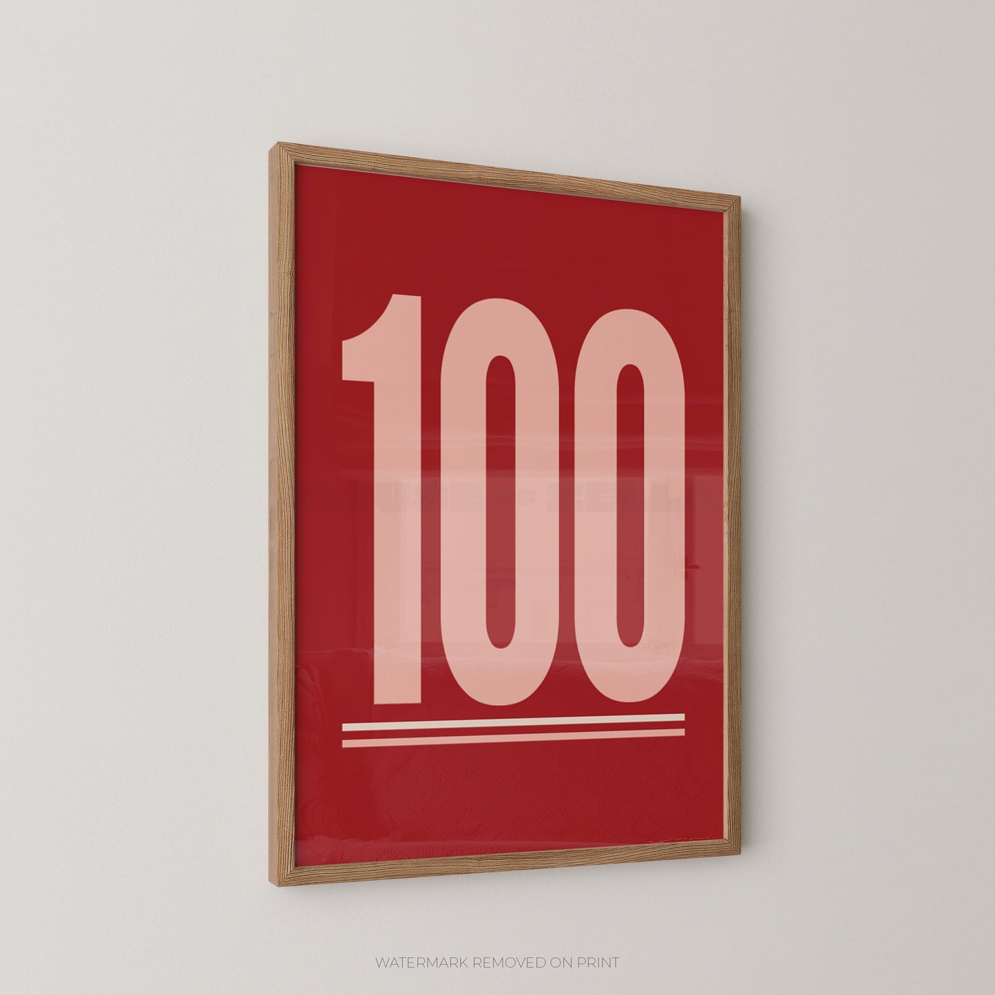 Framed wall art featuring the number 100 in large pale pink numerals on a bold red background, shown hanging on a light gray wall.