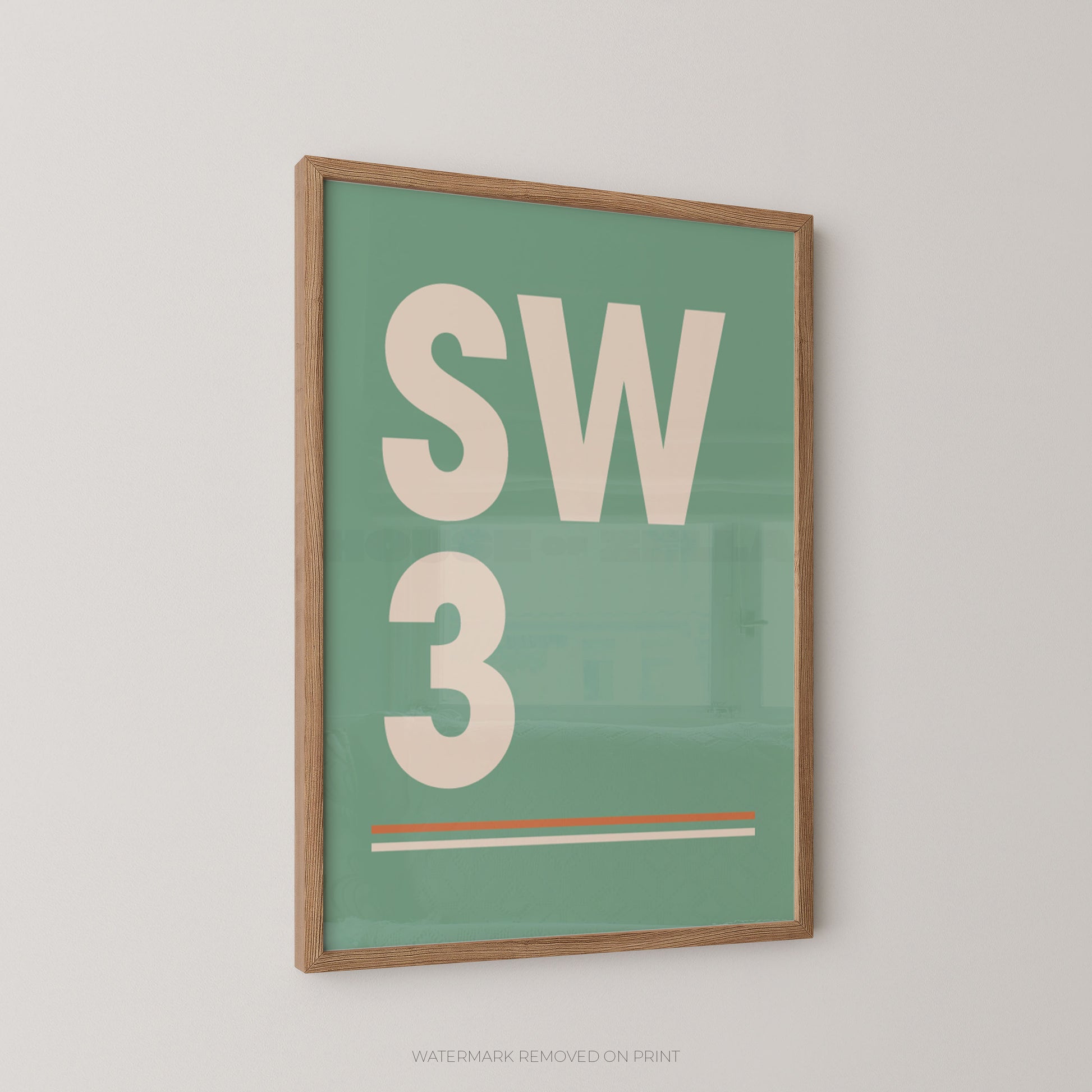 A wall art print in green and cream with a postcode displayed SW3 personalised design in an oak frame hung on a pale wall.
