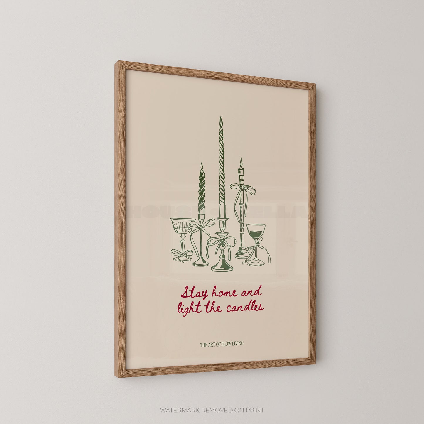 Framed art print featuring a minimalist illustration of candlesticks and glassware with the phrase 'Stay home and light the candles' in red script, shown hanging on a light gray wall.