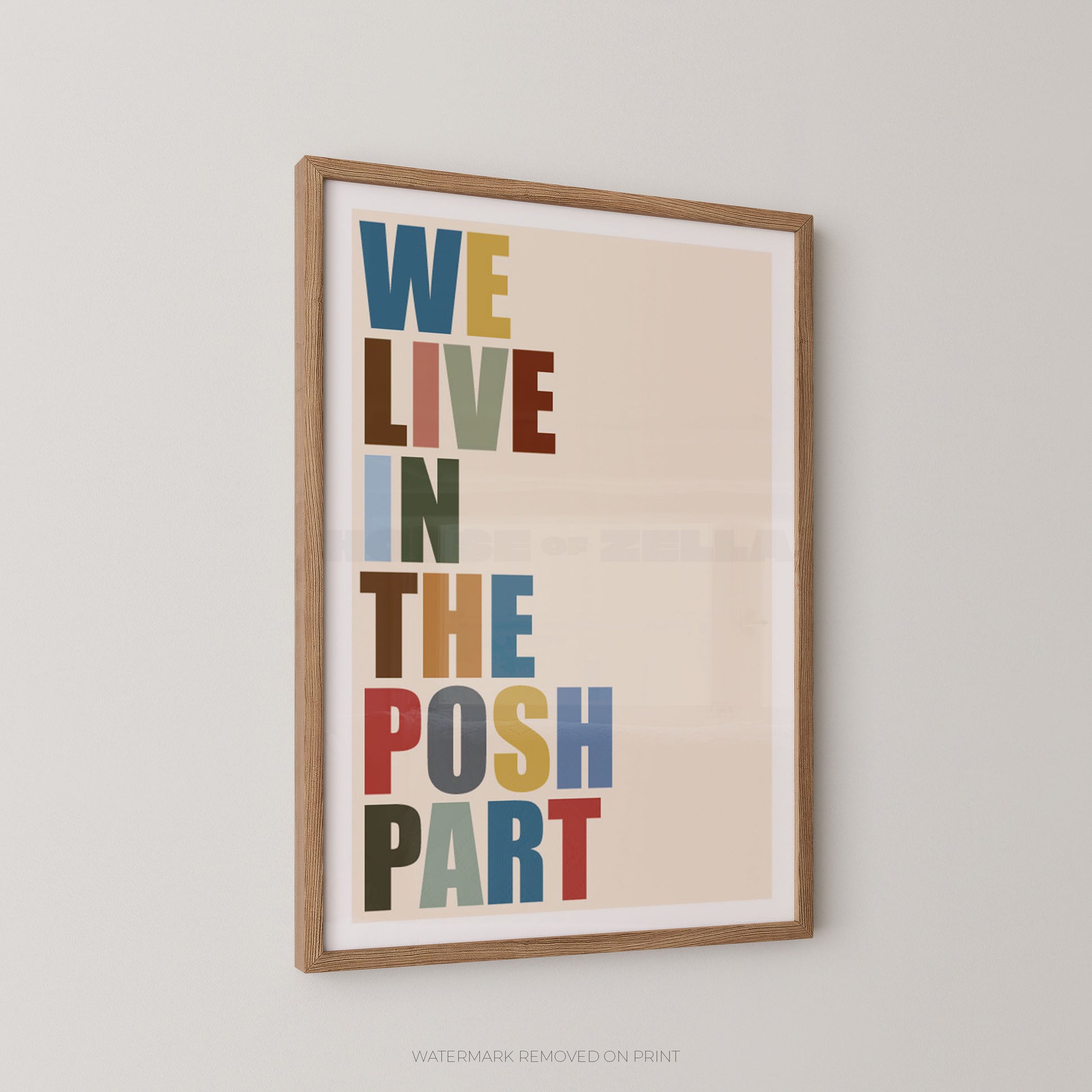 Framed typographic wall art hanging on a light gray wall, featuring the phrase “WE LIVE IN THE POSH PART” in large multicolored letters on a warm beige background.