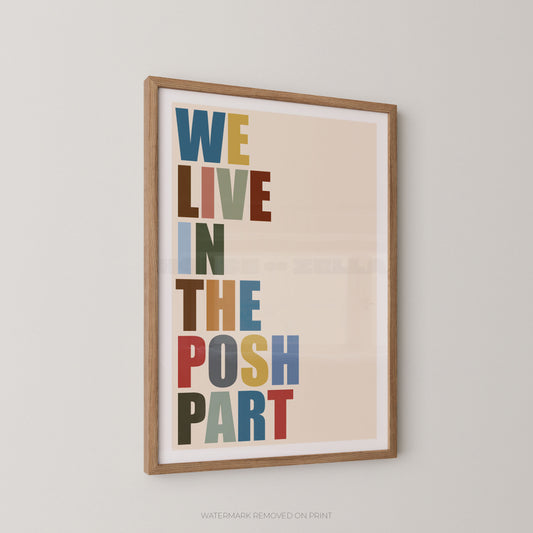 Framed typographic wall art hanging on a light gray wall, featuring the phrase “WE LIVE IN THE POSH PART” in large multicolored letters on a warm beige background.