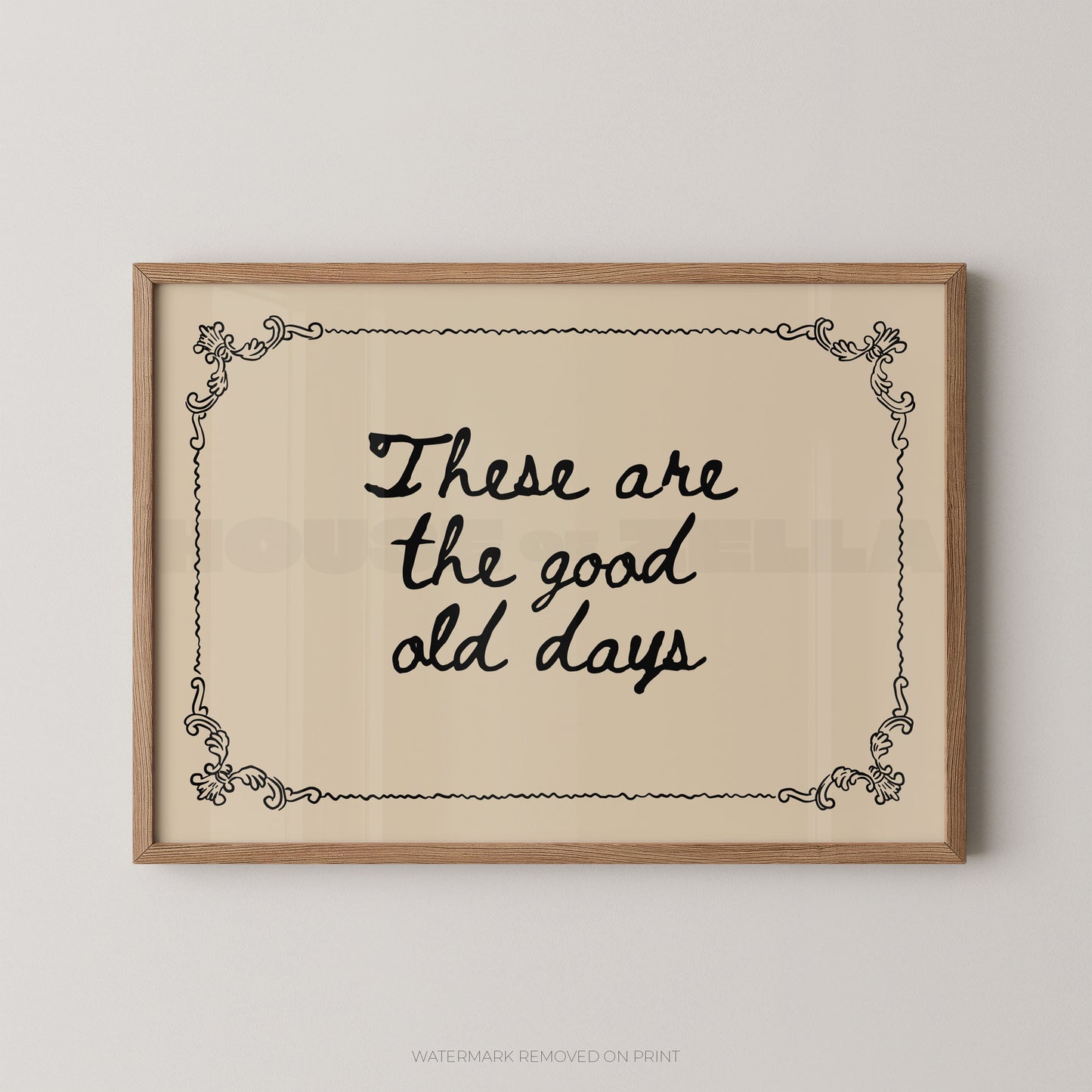 Framed wall art print with the phrase “These are the good old days” in black script on a warm cream background, bordered by a light wood frame and small decorative corner flourishes.