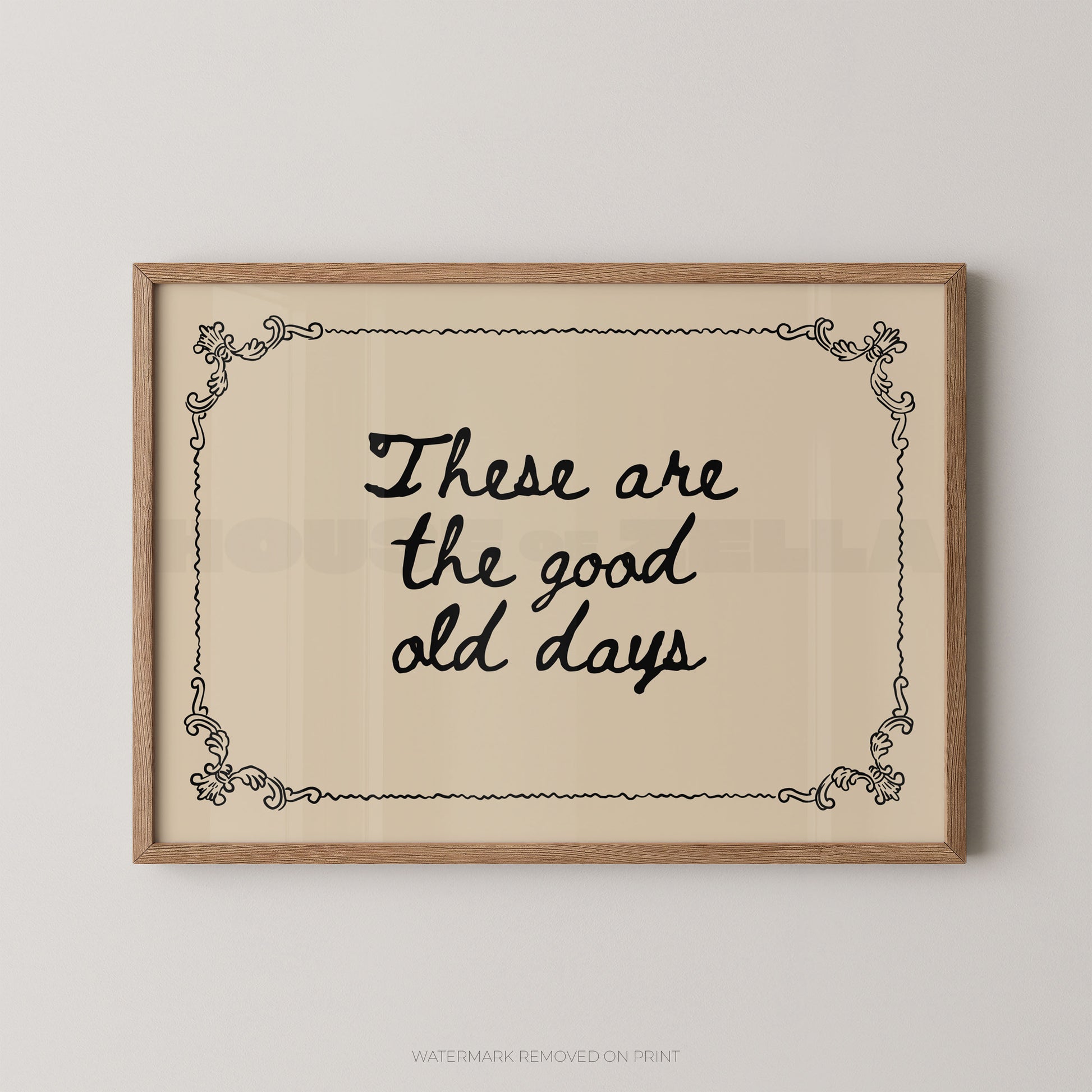 Framed wall art print with the phrase “These are the good old days” in black script on a warm cream background, bordered by a light wood frame and small decorative corner flourishes.