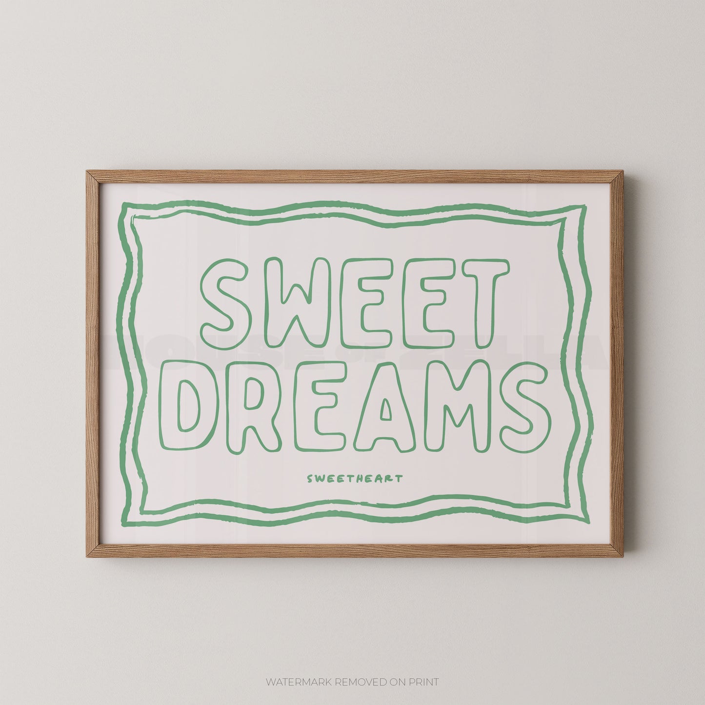 Framed typographic wall art reading “SWEET DREAMS” in green outline lettering on a white background, with a light wood frame and small “SWEETHEART” text below. The framed print is shown against a light neutral wall.