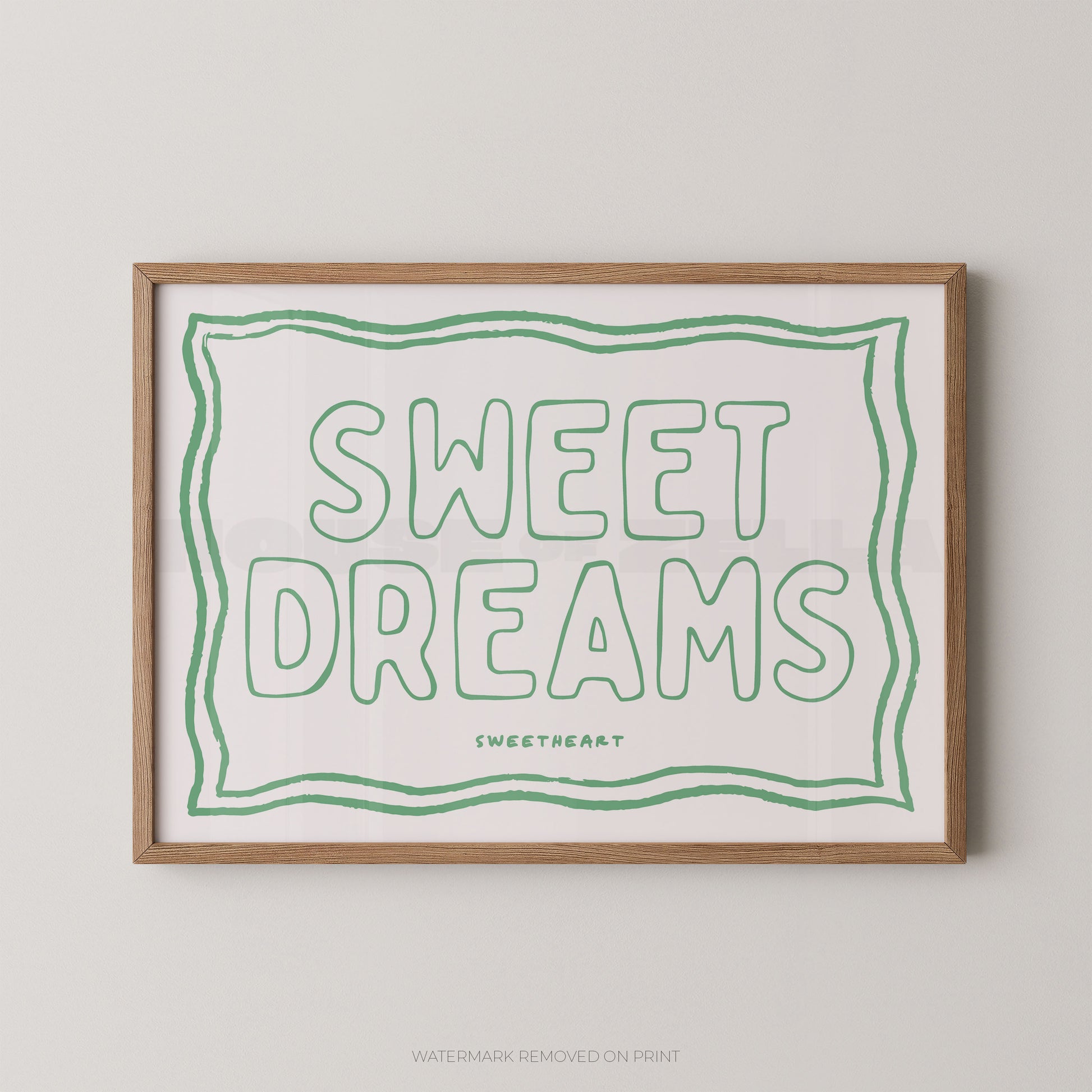 Framed typographic wall art reading “SWEET DREAMS” in green outline lettering on a white background, with a light wood frame and small “SWEETHEART” text below. The framed print is shown against a light neutral wall.