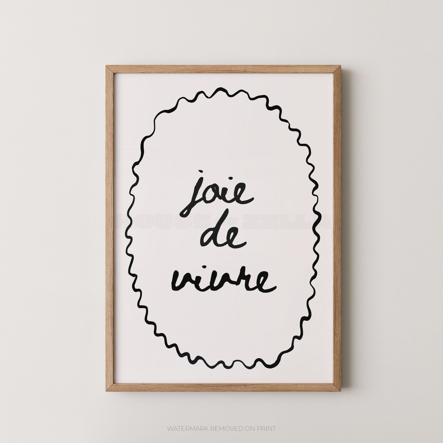 Framed wall art print with the French phrase “joie de vivre” in black script inside a black scalloped oval, shown in a light natural wood frame against a light gray wall.
