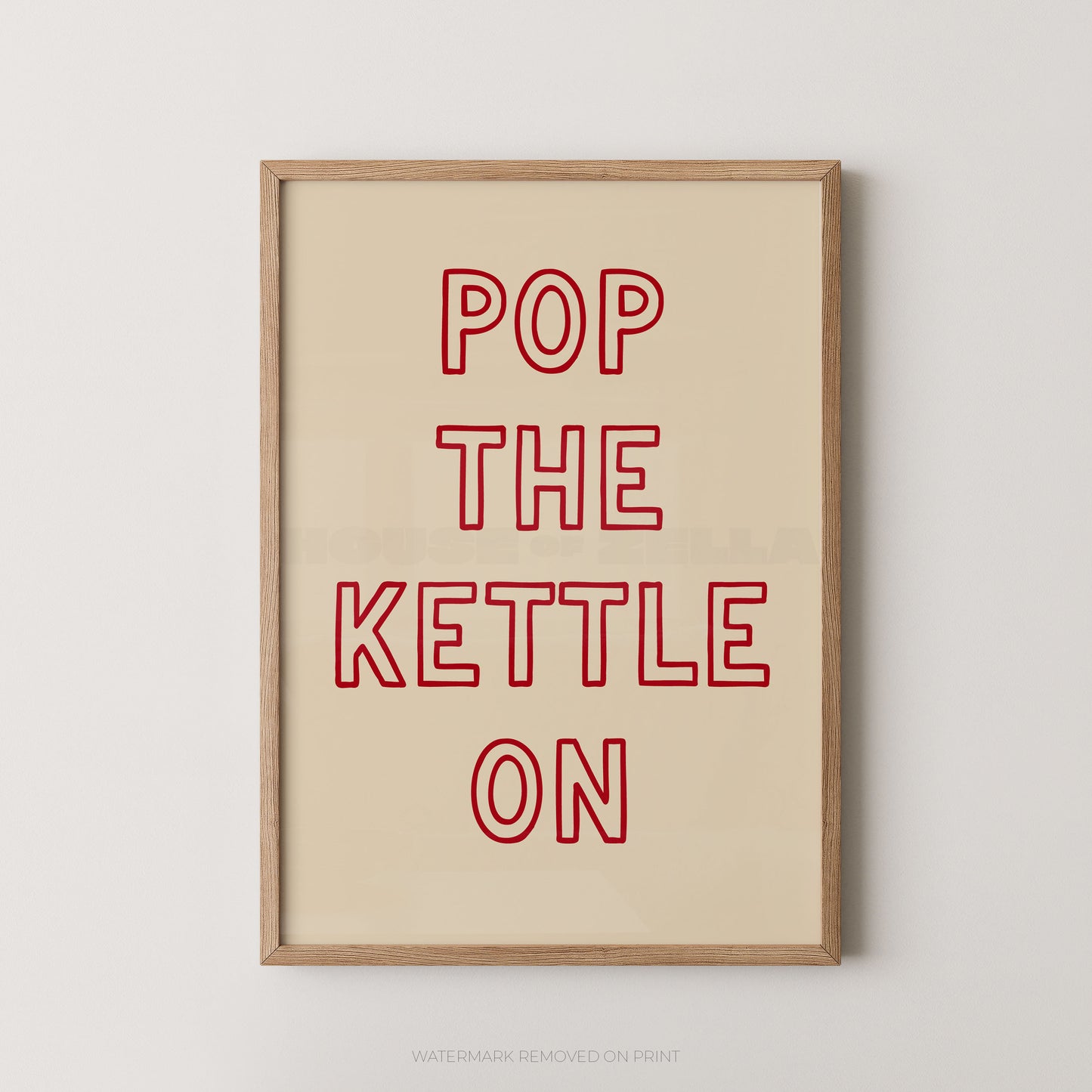 Framed typographic wall art with the phrase “POP THE KETTLE ON” in red outlined letters on a warm cream background, shown in a light wood frame against a light gray wall.