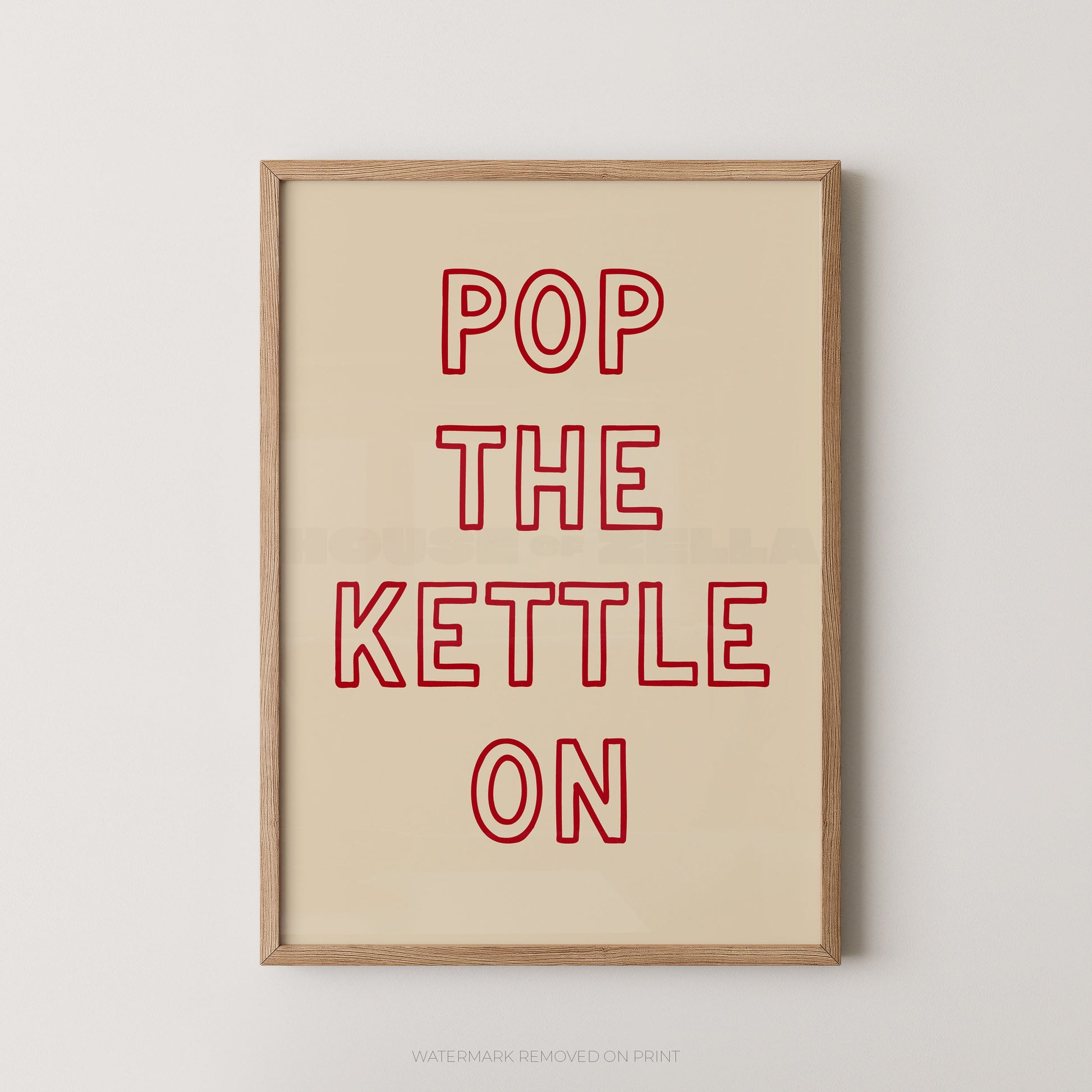 Framed typographic wall art with the phrase “POP THE KETTLE ON” in red outlined letters on a warm cream background, shown in a light wood frame against a light gray wall.