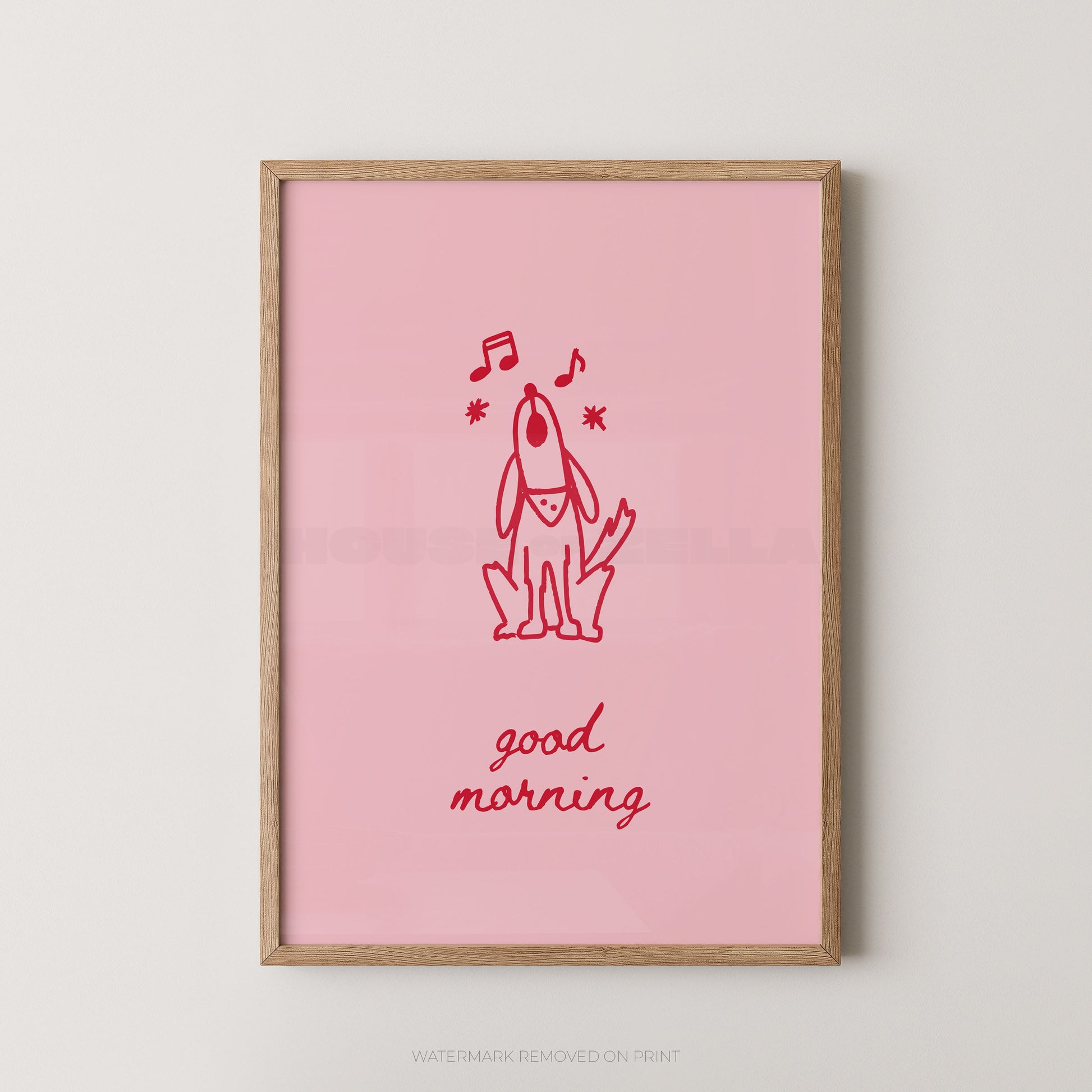 A framed art print featuring a pink background with a red line drawing of a dog, musical notes, and the words 'good morning' in red script, displayed against a light gray wall.