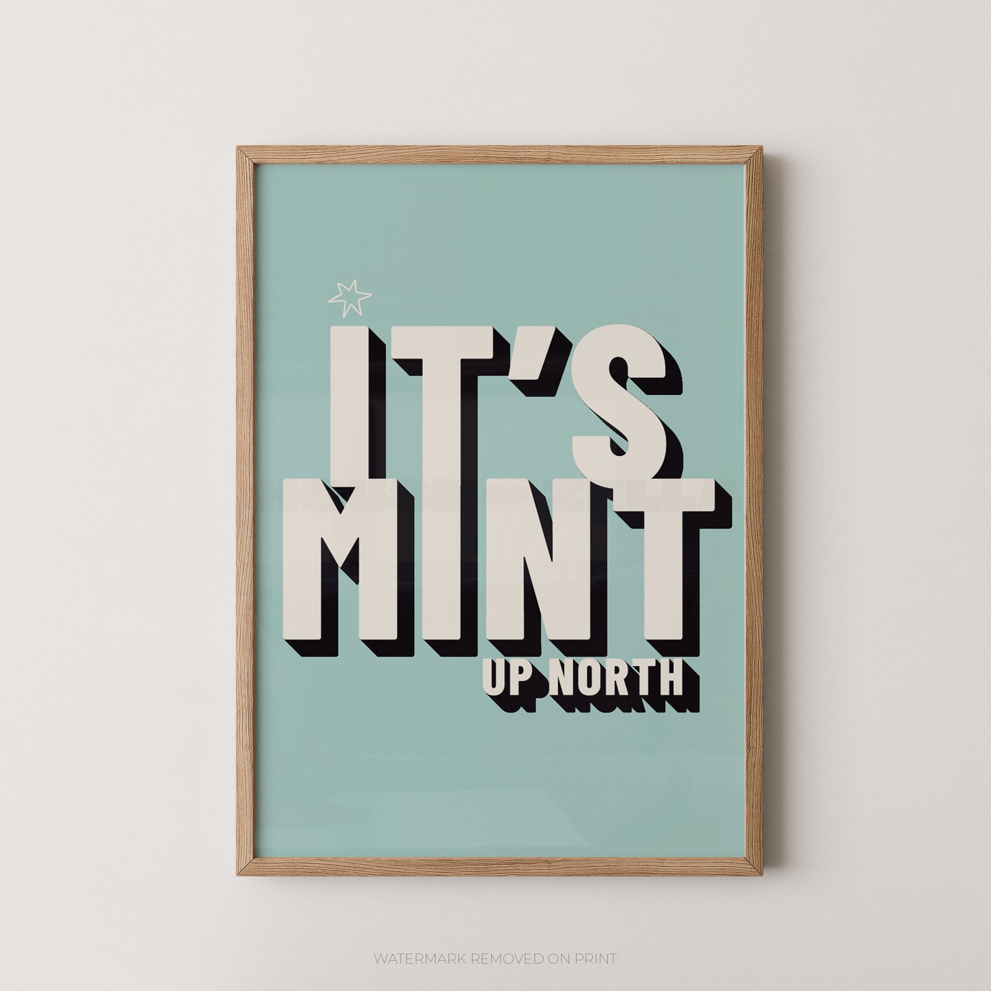 Framed typographic wall art hanging on a light neutral wall. The print has a pale aqua background with large cream lettering reading “IT’S MINT” and smaller cream text reading “UP NORTH,” plus a small star near the top left.