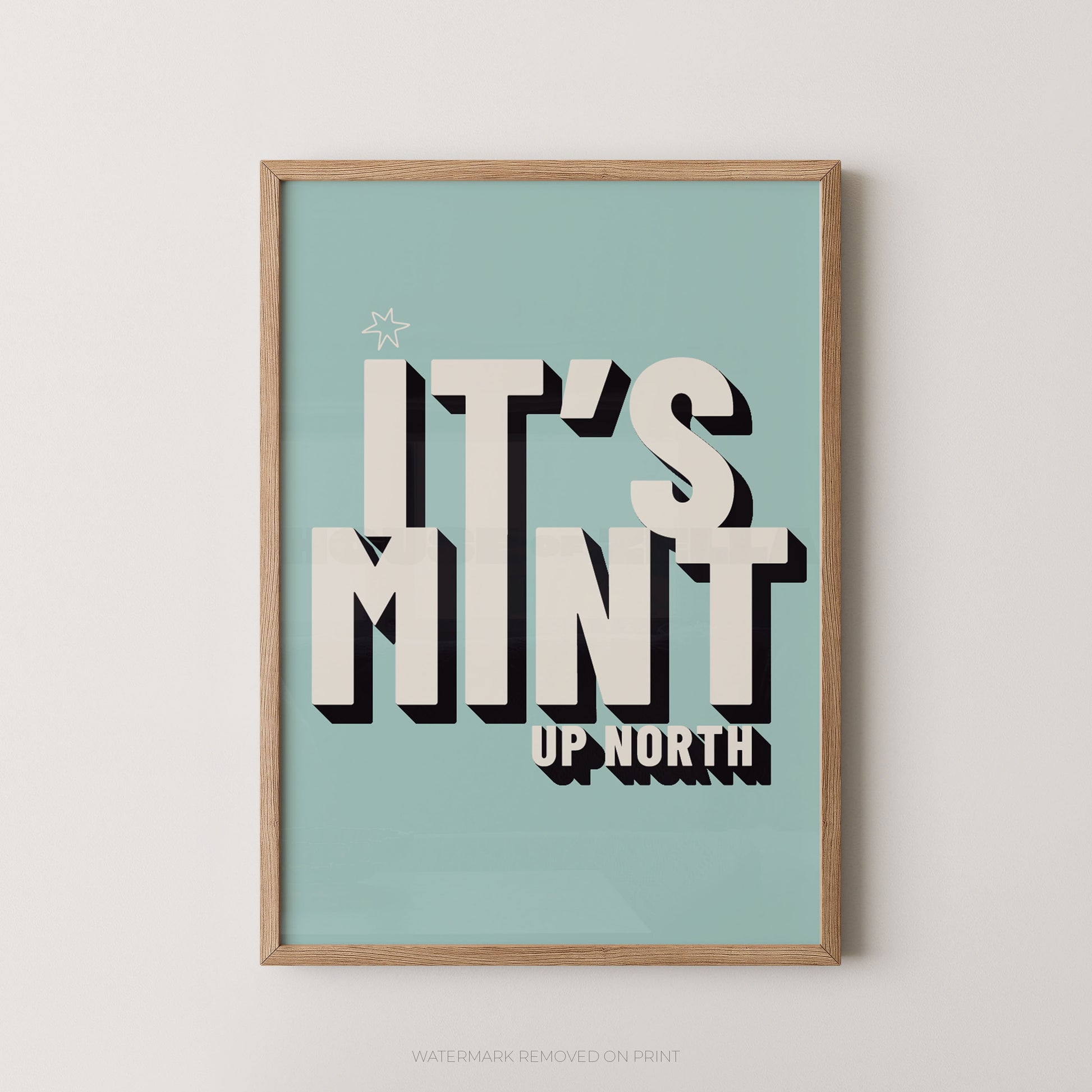 Framed typographic wall art hanging on a light neutral wall. The print has a pale aqua background with large cream lettering reading “IT’S MINT” and smaller cream text reading “UP NORTH,” plus a small star near the top left.
