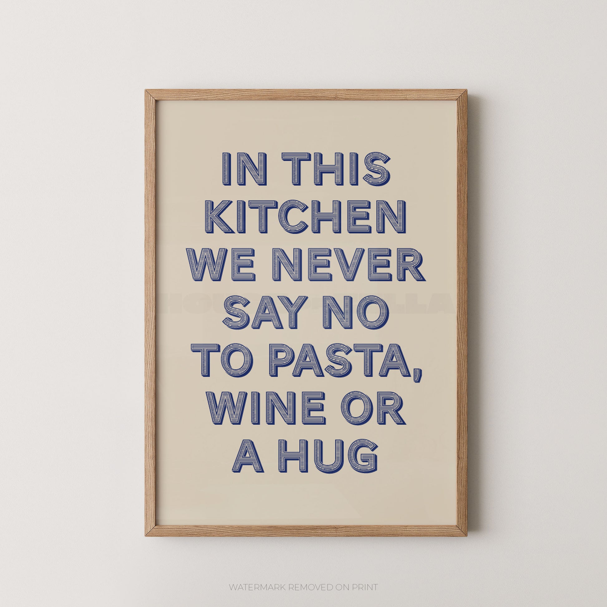 A framed typographic wall art print with the phrase “IN THIS KITCHEN WE NEVER SAY NO TO PASTA, WINE OR A HUG” in blue raised letters on a warm cream background, shown against a light neutral wall.
