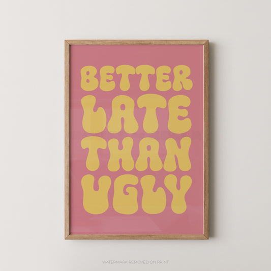 A framed typographic wall art print with the phrase “BETTER LATE THAN UGLY” in large yellow retro letters on a pink background, shown hanging against a light neutral wall.