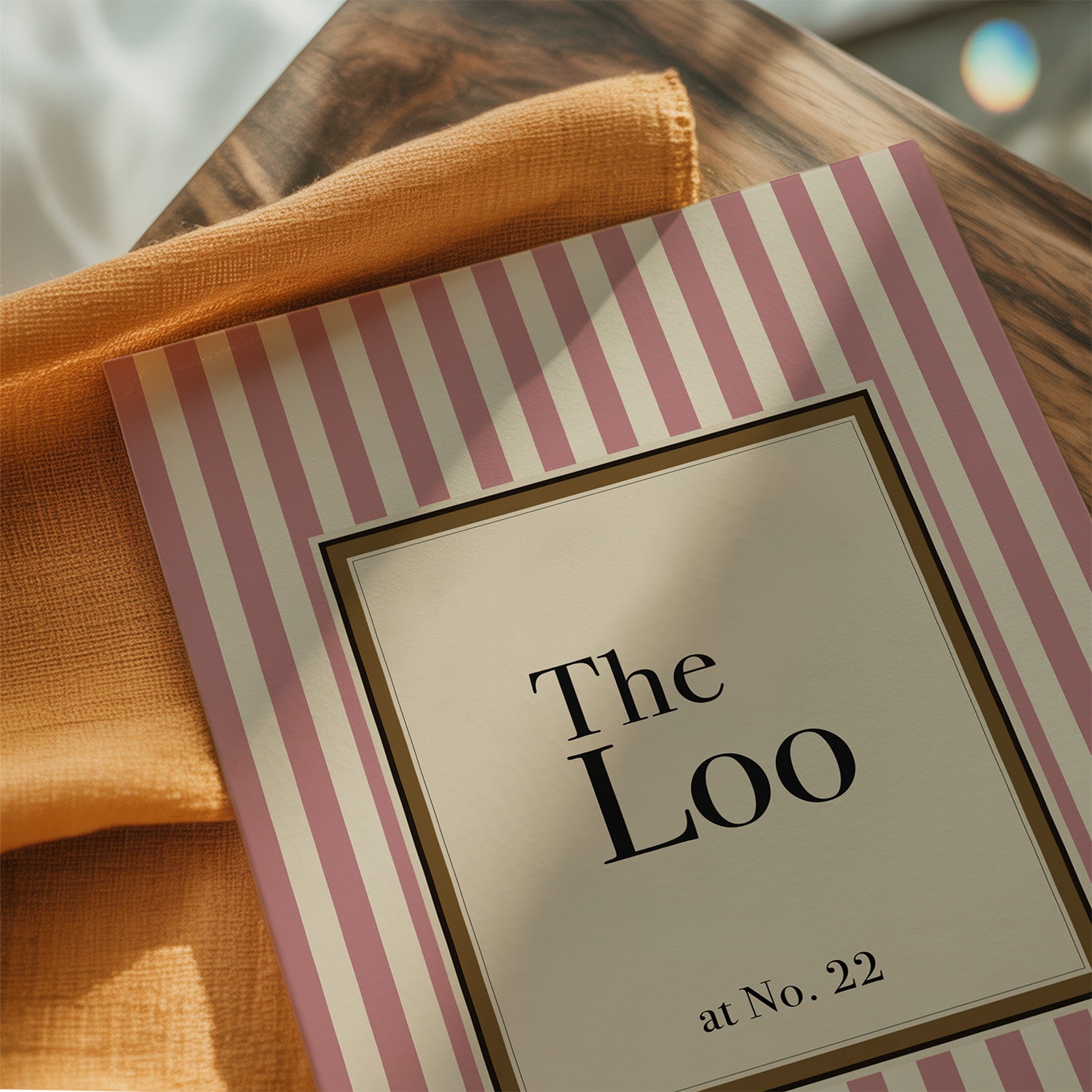 Striped paper with 'The Loo at No. 22' text on a wooden surface with an orange cloth.