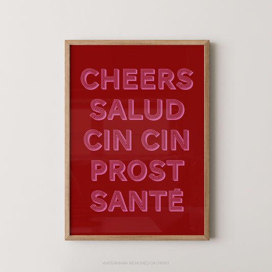 Framed wall art print with the phrase 'CHEERS SALUD CIN CIN PROST SANTÉ' in pink neon-style outlined lettering on a deep red background, shown in a light wood frame against a light gray wall.
