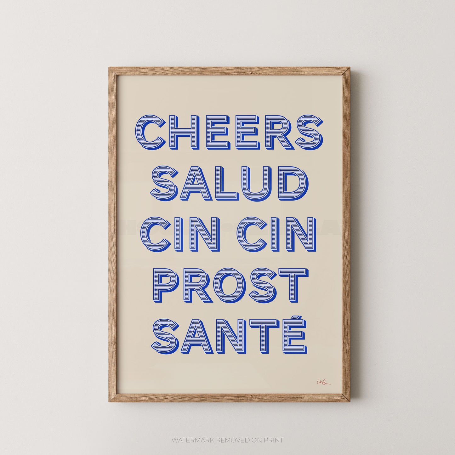 Framed typographic wall art print with the phrase “CHEERS SALUD CIN CIN PROST SANTÉ” in blue outlined letters on a warm cream background, shown in a light natural wood frame against a light gray wall.