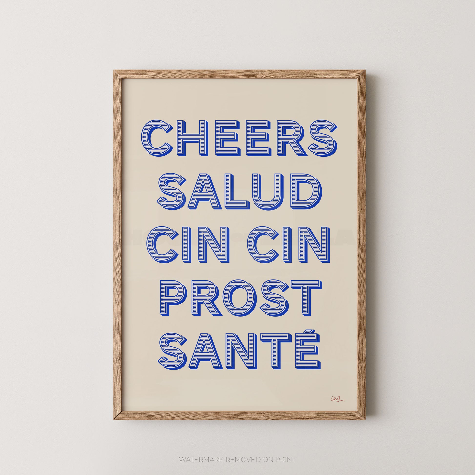 Framed typographic wall art print with the phrase “CHEERS SALUD CIN CIN PROST SANTÉ” in blue outlined letters on a warm cream background, shown in a light natural wood frame against a light gray wall.