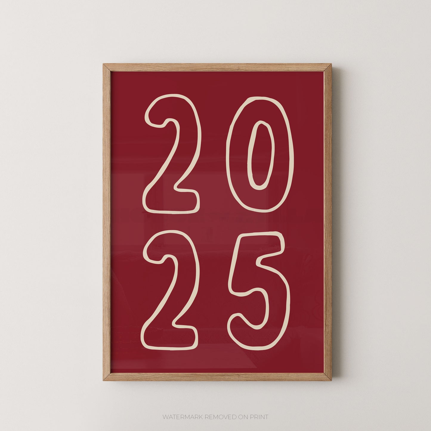 Framed wall art print with the numbers '2025' in cream outline on a deep red background, shown hanging against a light neutral wall.
