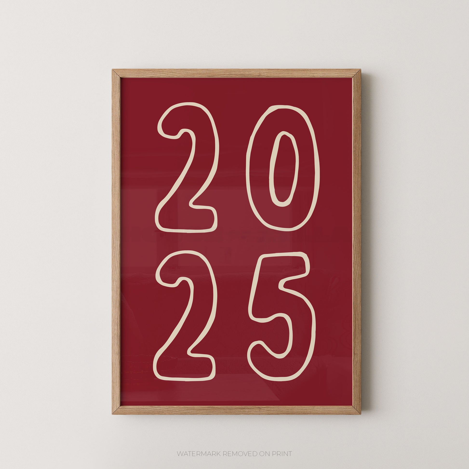 Framed wall art print with the numbers '2025' in cream outline on a deep red background, shown hanging against a light neutral wall.