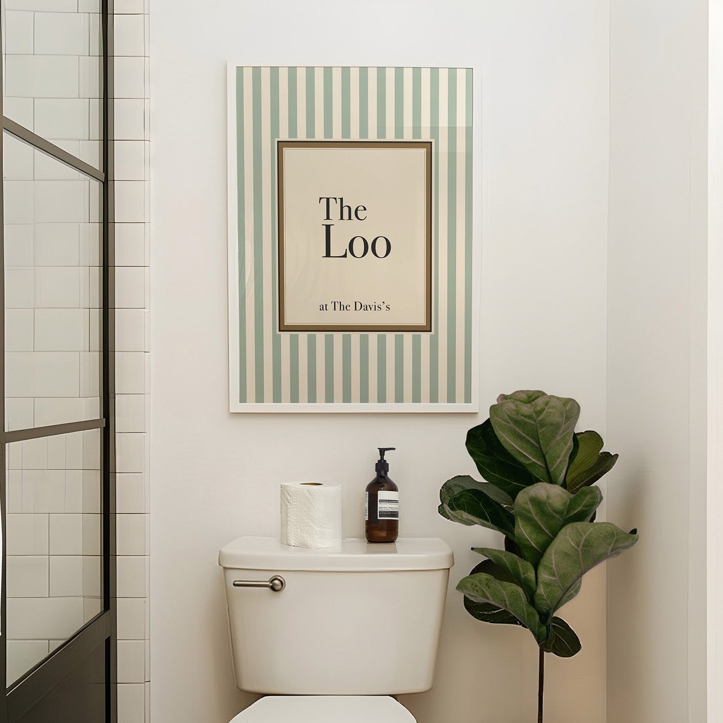 Bathroom with a toilet, plant, and framed picture on the wall.