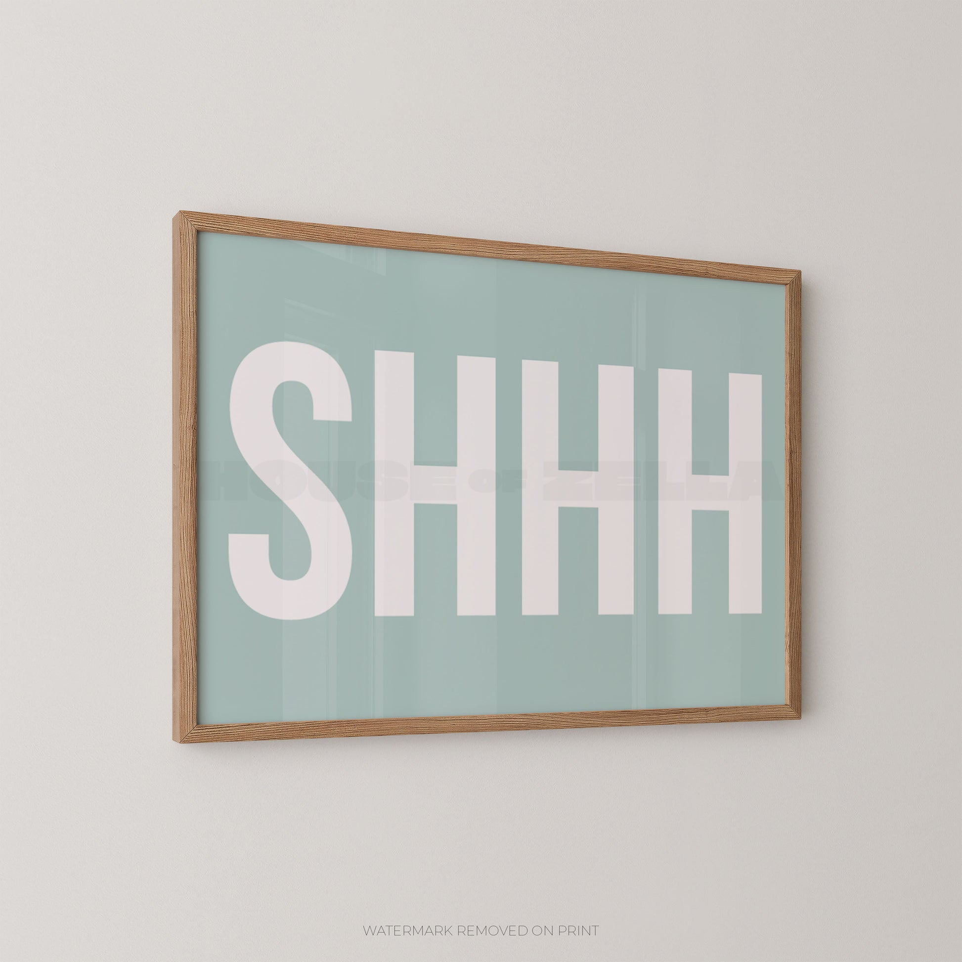 Framed wall art print with the word 'SHHH' in large white letters on a pale mint background, shown hanging on a light gray wall.
