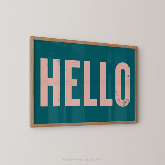 Framed wall art print with the word "HELLO" in large distressed pink letters on a teal background, shown hanging on a light gray wall.