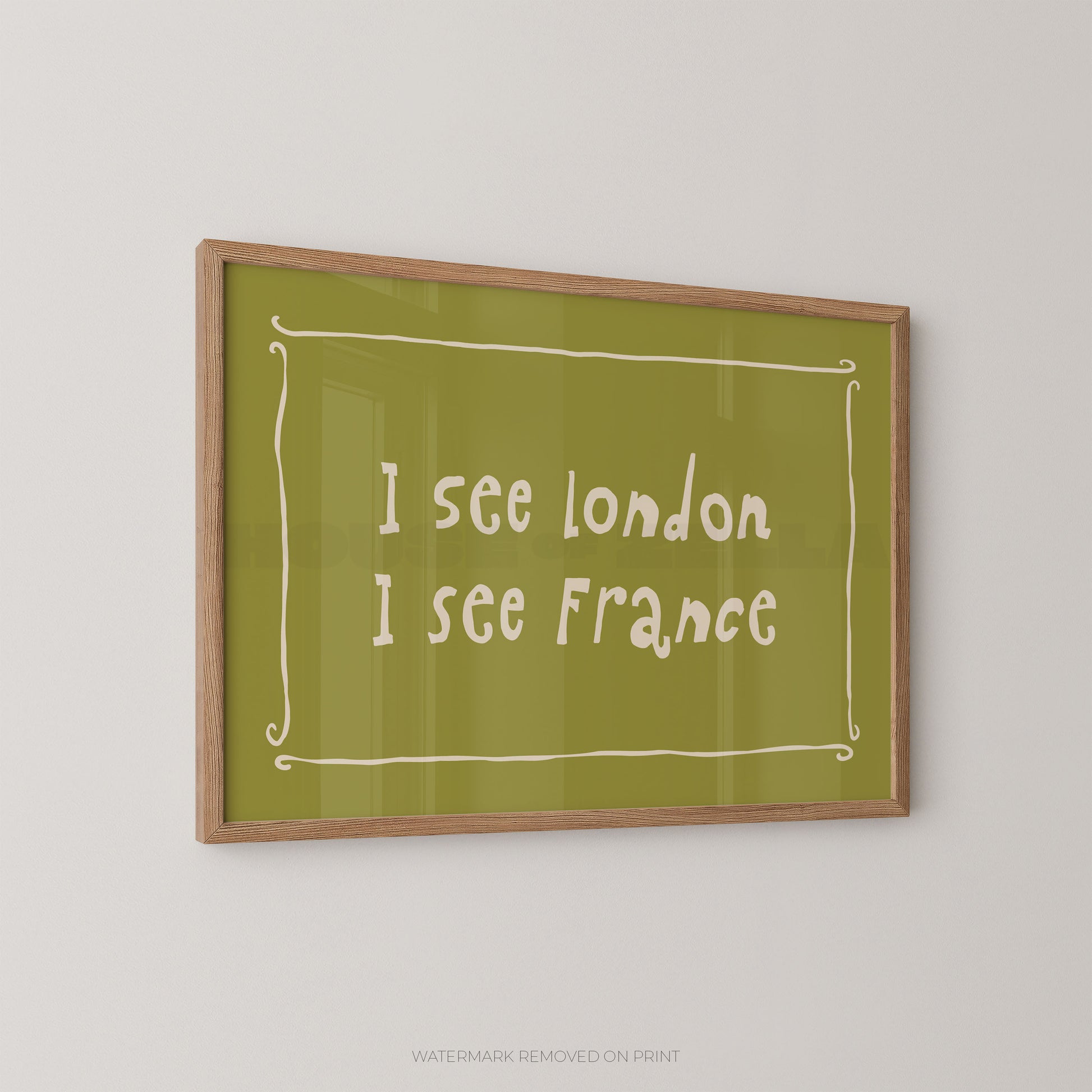 A framed typographic wall art print hanging on a light gray wall. The print has an olive green background with white handwritten-style text reading 'I see london I see france' inside a white decorative border, and a light natural wood frame.