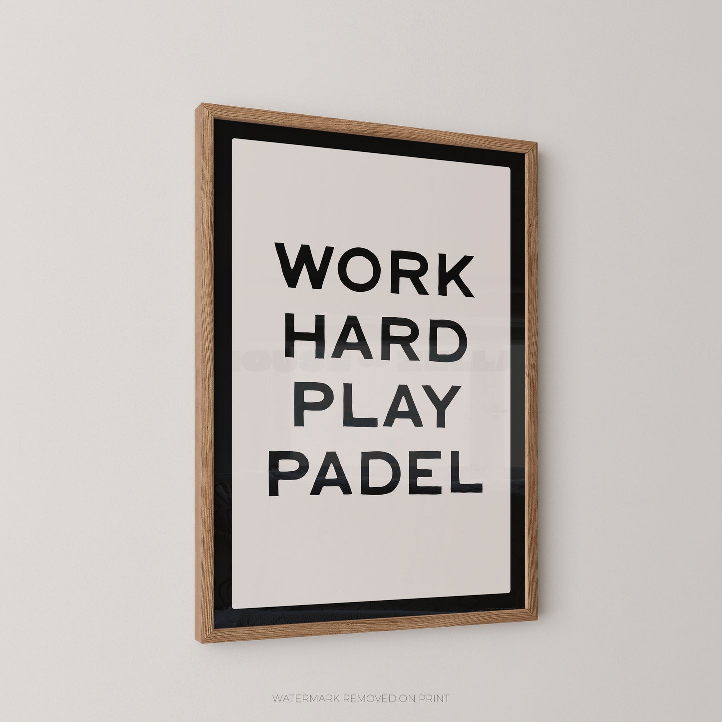 "Work Hard Play Padel bold typography sports wall art print with black lettering on a cream background with a black border, displayed at an angle in an oak frame"

