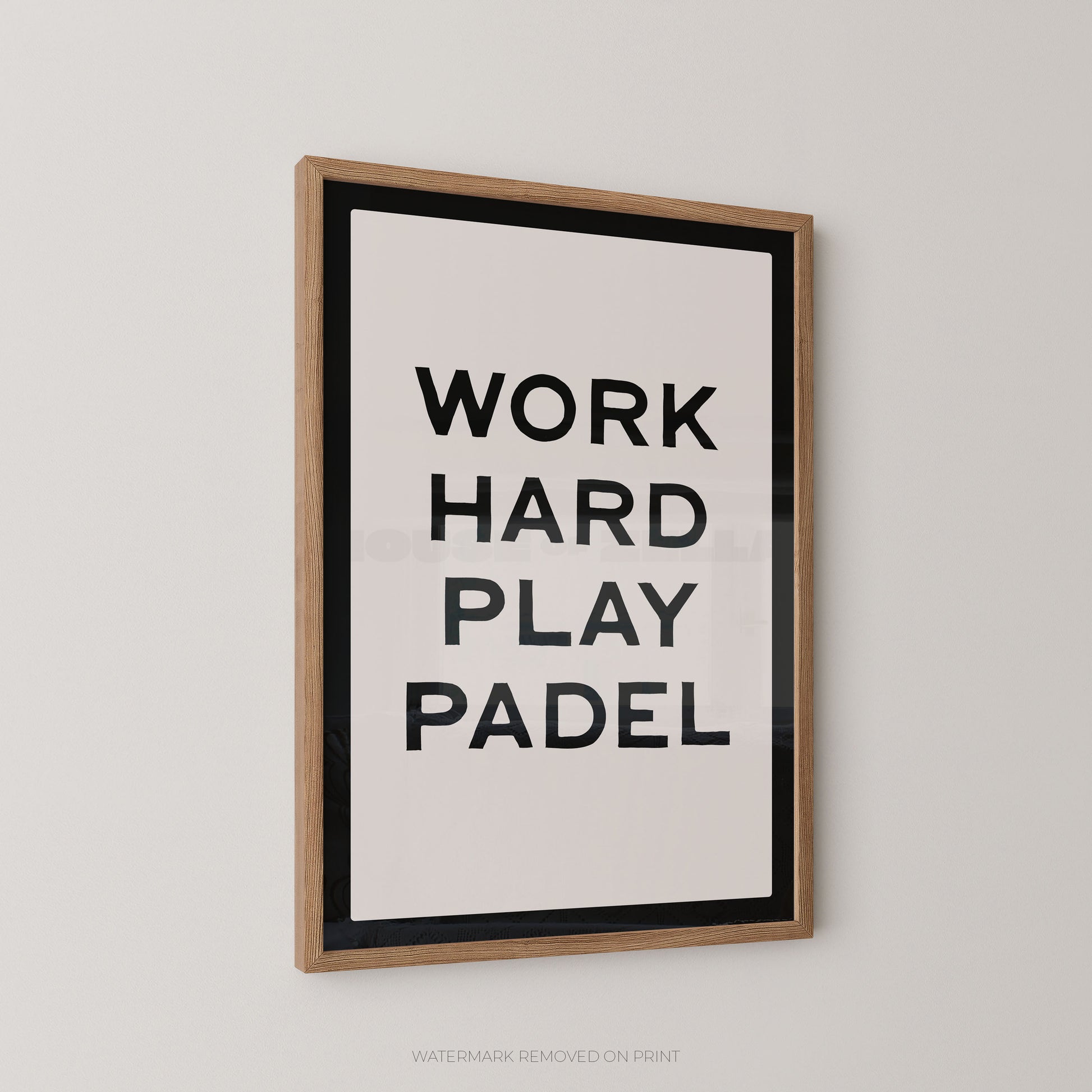 "Work Hard Play Padel bold typography sports wall art print with black lettering on a cream background with a black border, displayed at an angle in an oak frame"


