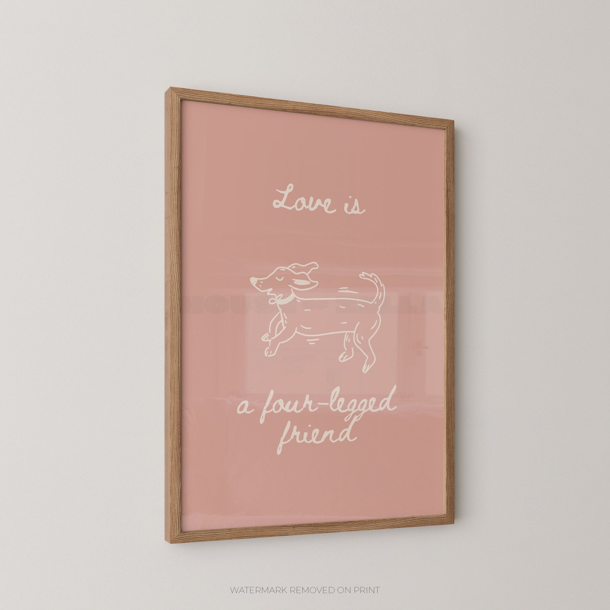 A framed art print with a dusty pink background, featuring a white line drawing of a dog and the text 'Love is a four-legged friend' in white script, enclosed in a light wood frame.