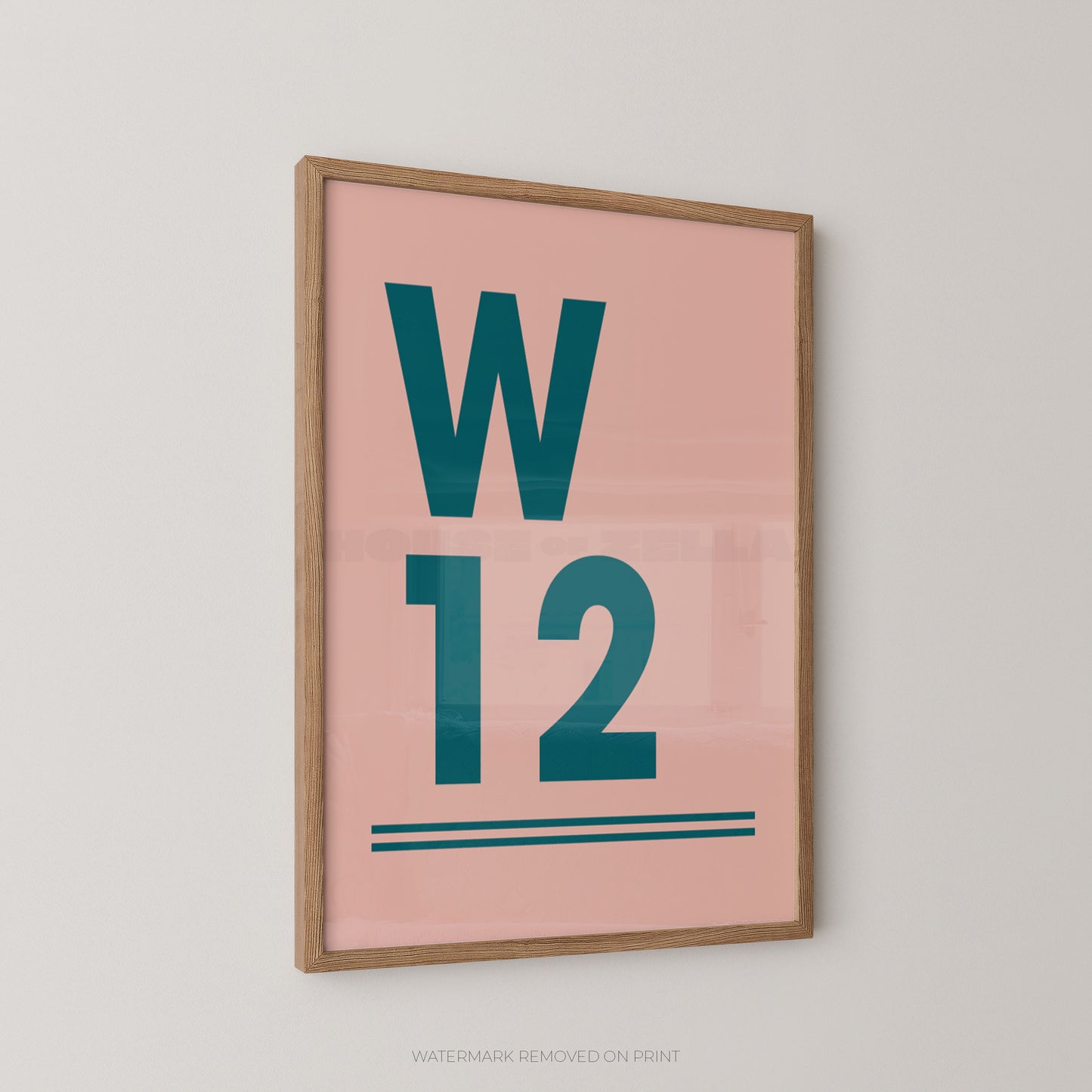 A framed minimalist typographic postcode wall art print featuring a pink background with large teal letters 'W' and '12' and two teal horizontal lines, shown hanging on a light gray wall.