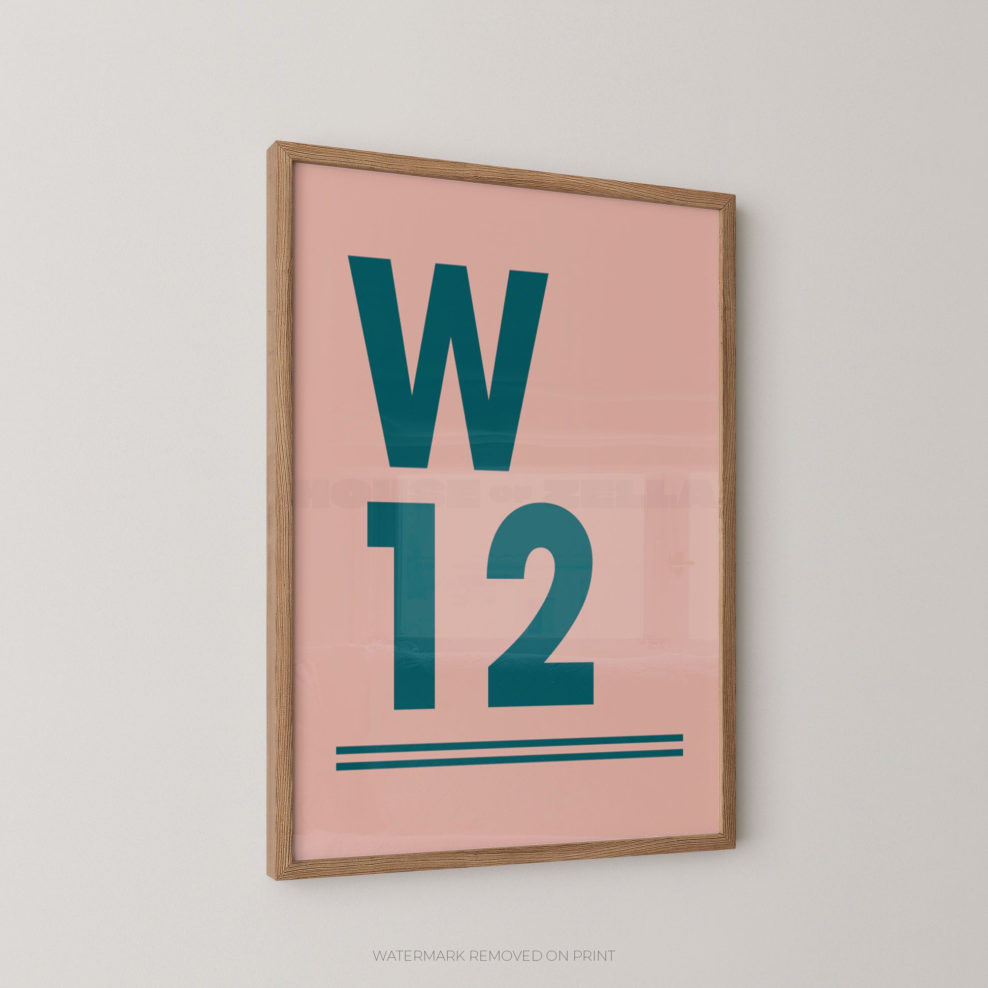 A framed minimalist typographic postcode wall art print featuring a pink background with large teal letters 'W' and '12' and two teal horizontal lines, shown hanging on a light gray wall.