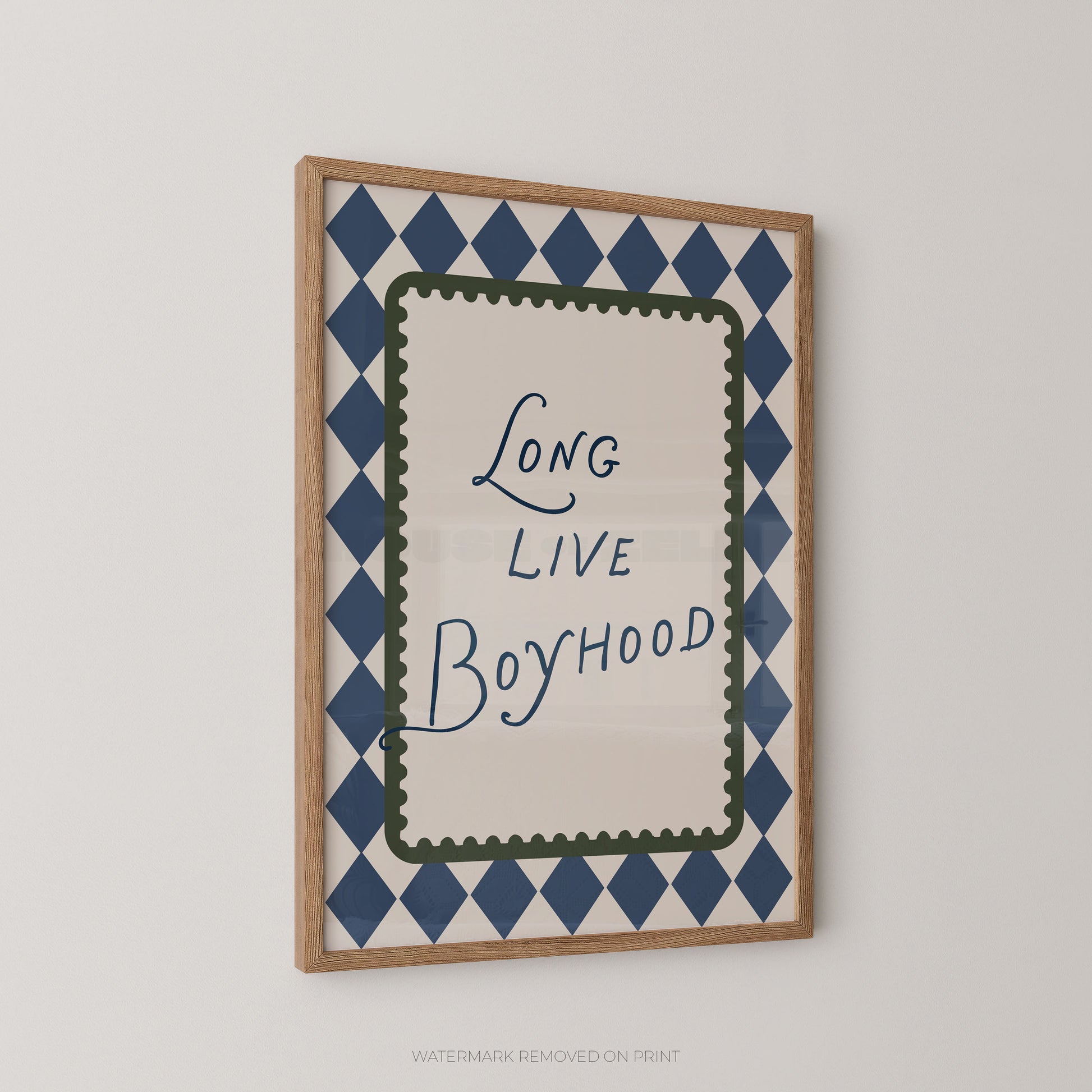 Framed wall art print with the phrase 'Long Live Boyhood' in blue script, surrounded by a navy and white diamond pattern and a green inner border, shown in a light wood frame against a light gray wall.