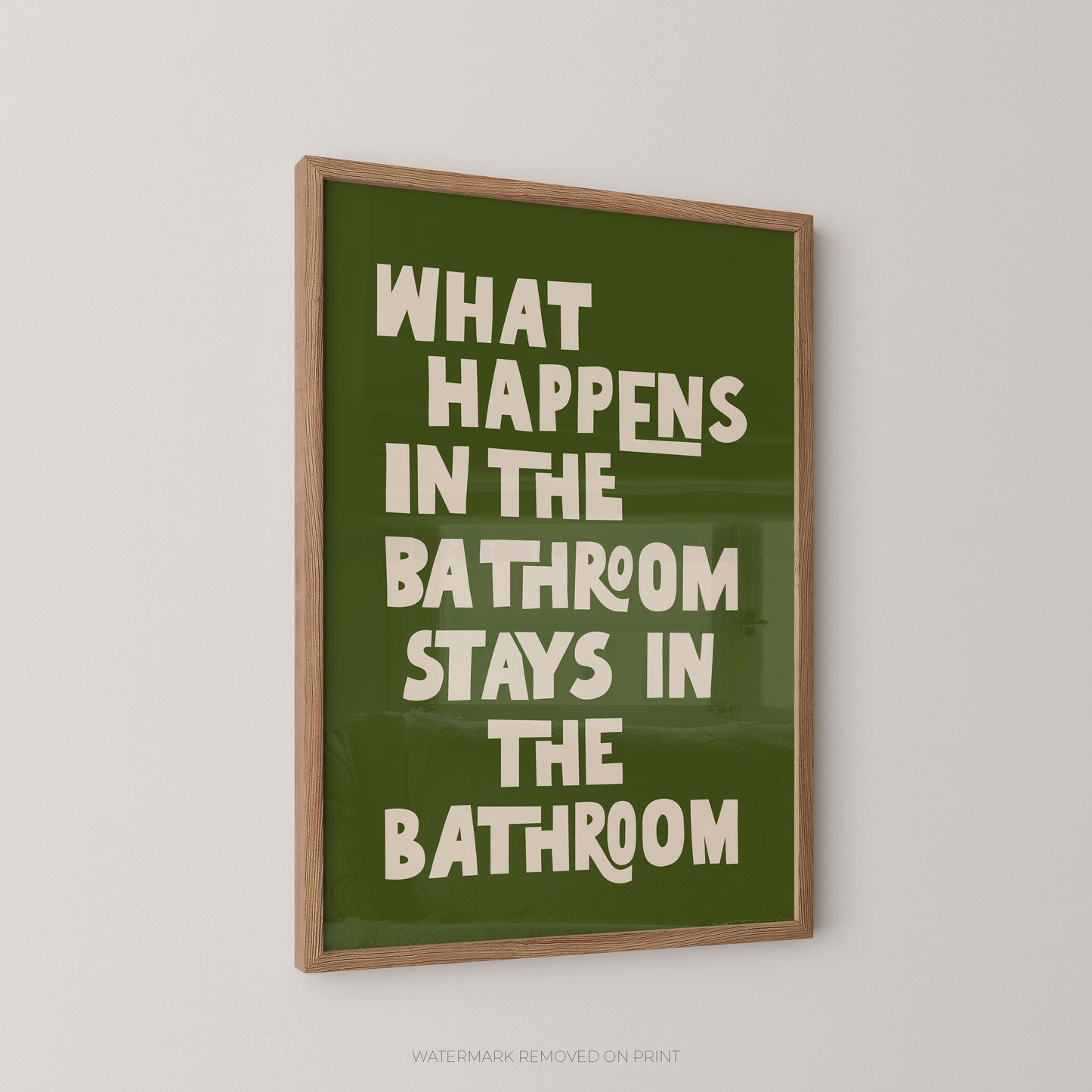 Funny bathroom wall art print in a wood frame – playful chunky cream typography on a green background reading "What Happens In The Bathroom Stays In The Bathroom"