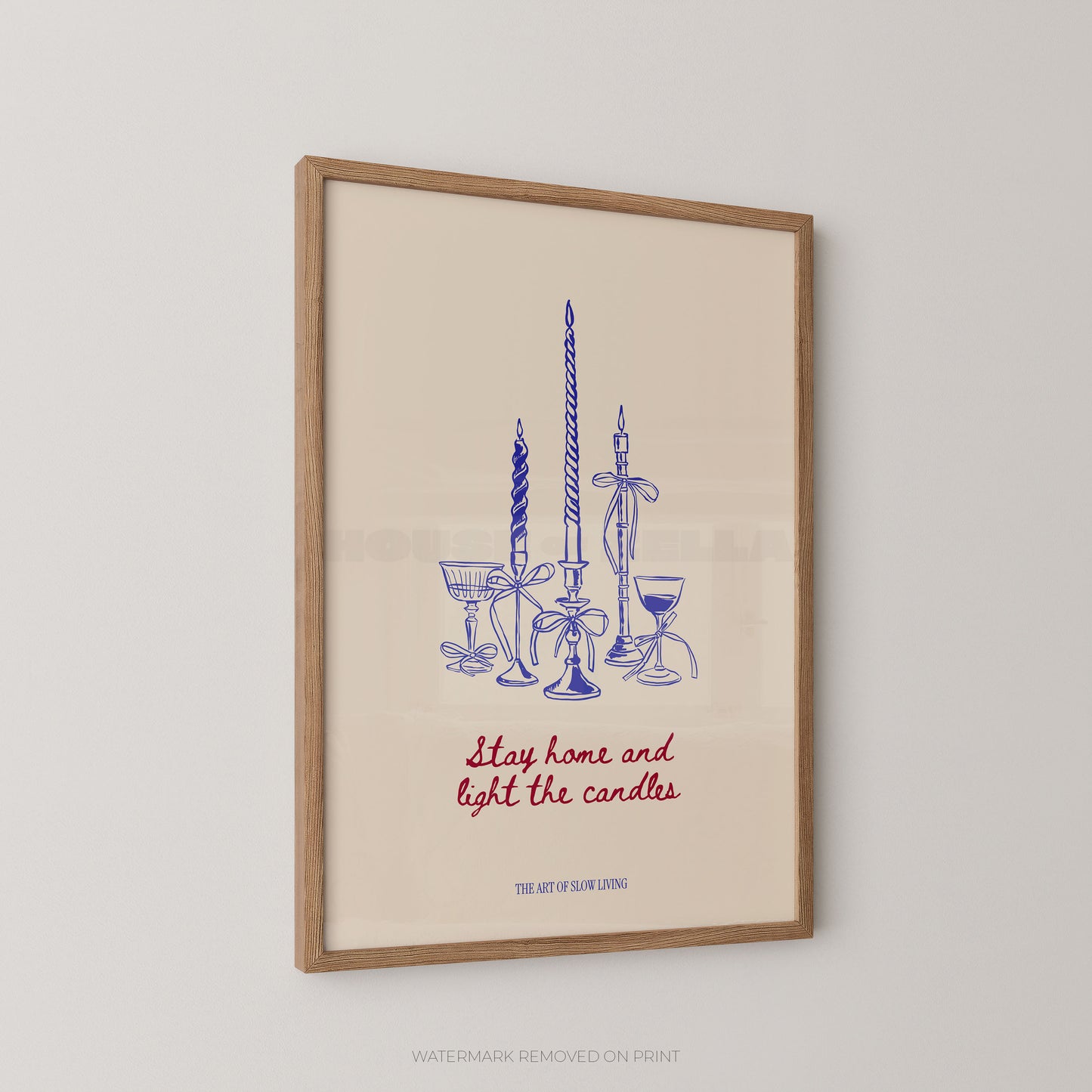 Framed art print featuring a blue line drawing of candlesticks and glassware with the phrase 'Stay home and light the candles' in red script, hanging on a light gray wall.