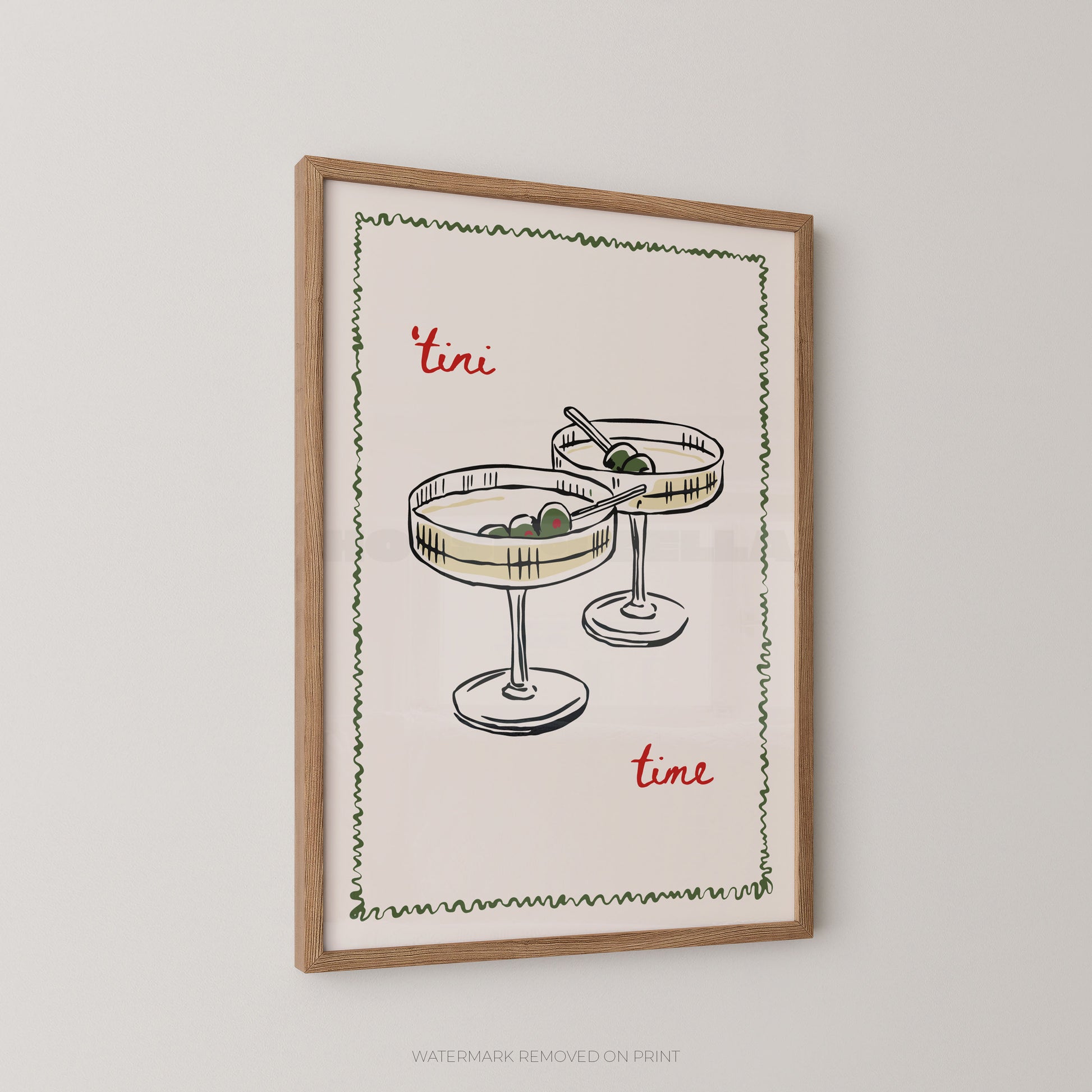 Framed wall art print featuring a hand-drawn illustration of two margarita glasses with olives, bordered by a green zigzag line, with the words "tini time" in red script on a cream background, shown in a light wood frame against a light gray wall.