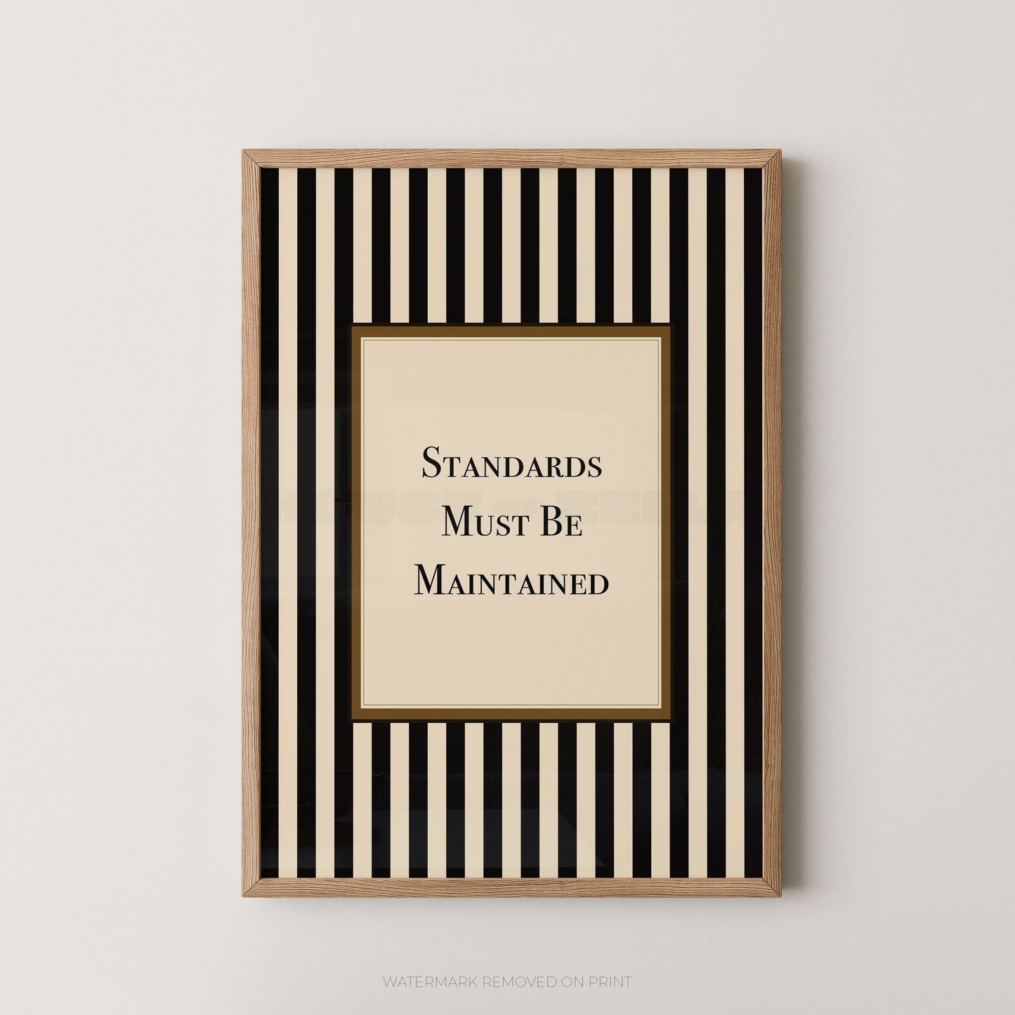 Framed wall art print with vertical black and cream stripes, a central cream panel, and the text 'STANDARDS MUST BE MAINTAINED' in black serif lettering, shown against a light neutral wall.